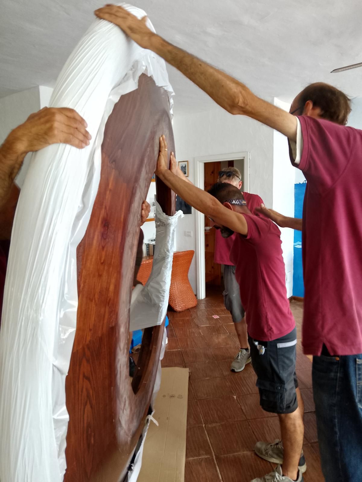 Quattro persone spostano all'interno un grande oggetto di legno imballato.