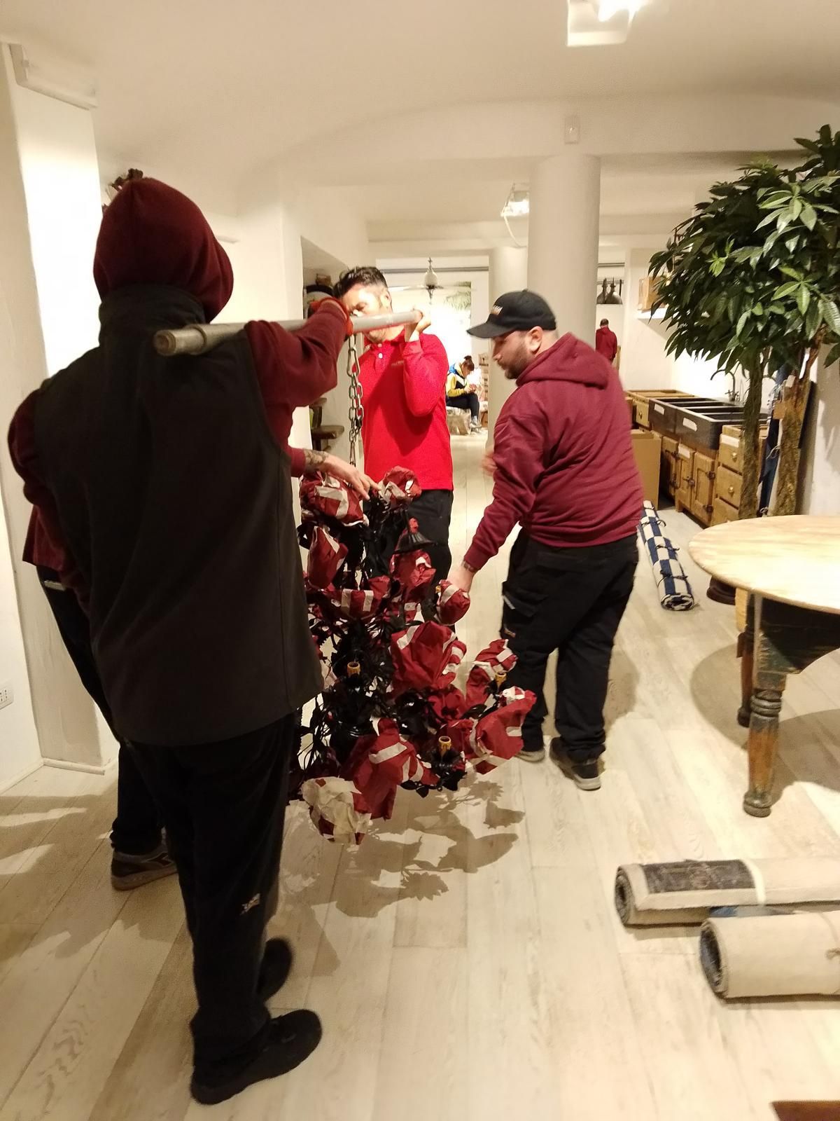Tre persone, vestite di rosso e nero, allestiscono un albero di Natale decorato in casa.