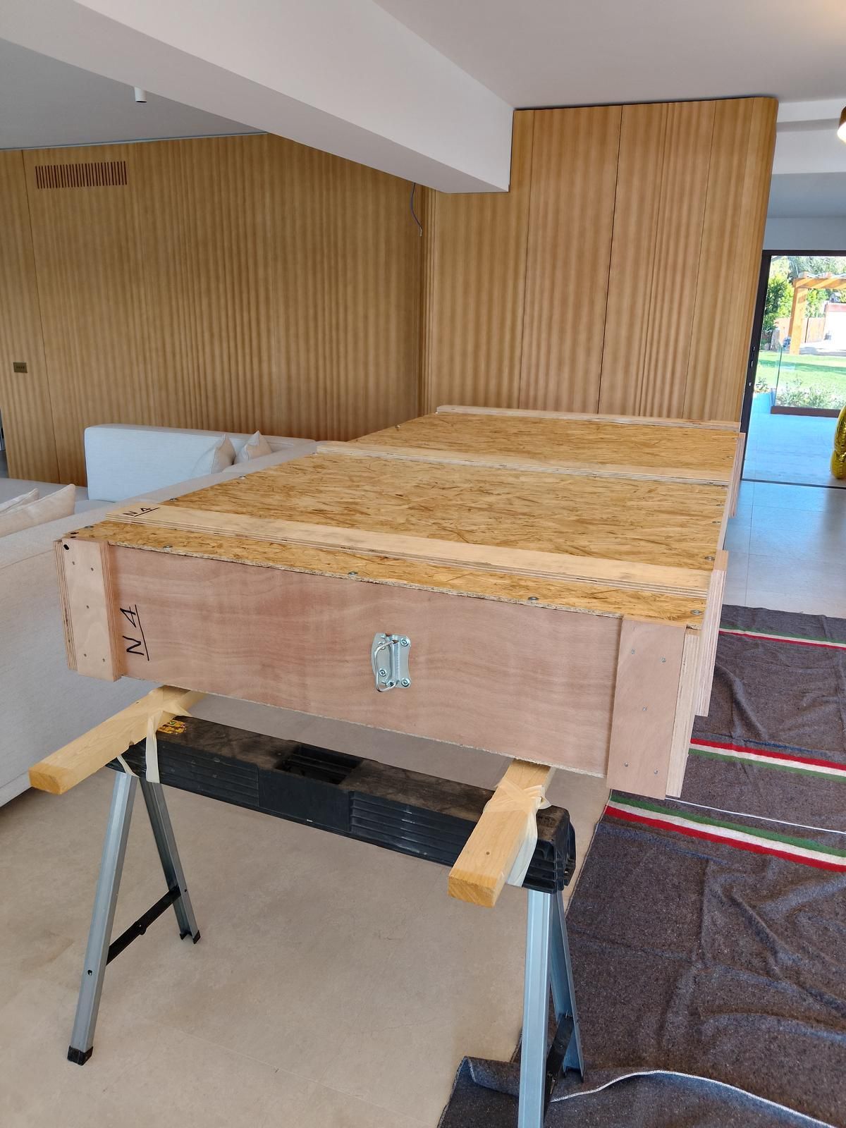 Cassa di legno su un cavalletto nero, all'interno, vicino a pannelli di legno e un tappeto.