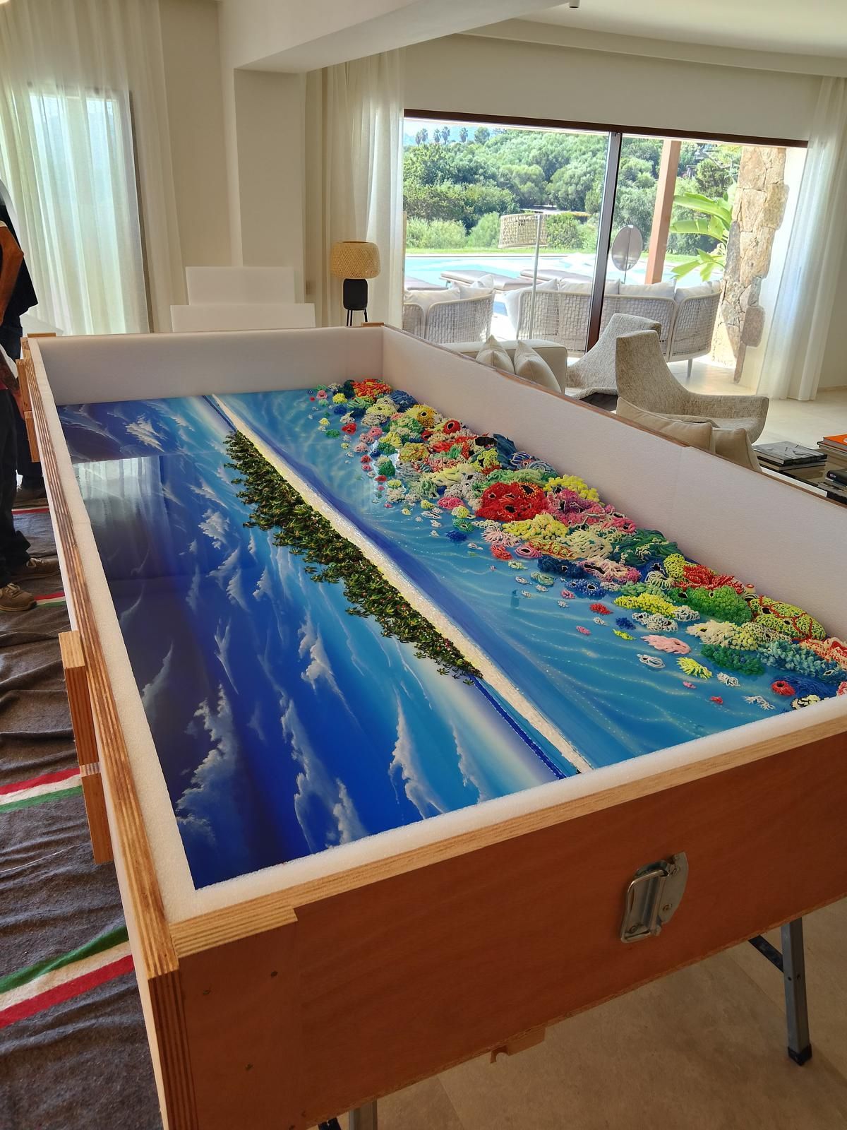 Un grande mosaico colorato raffigurante un oceano e una costa, in una cornice di legno, in un interno luminoso.