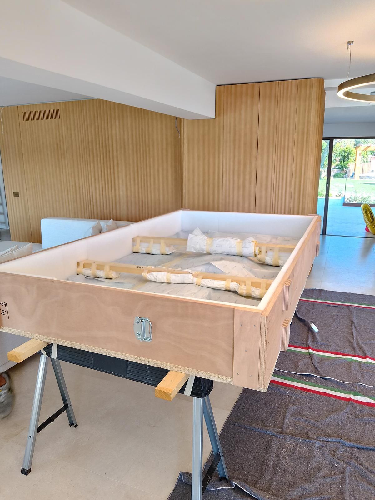 Cassa di legno su cavalletti, parzialmente costruita con materiale isolante, all'interno di una stanza con pannelli di legno.