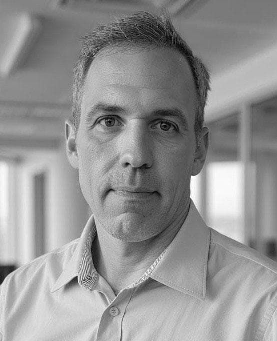 Man with short hair in a light-colored button-down shirt, neutral expression, indoors.