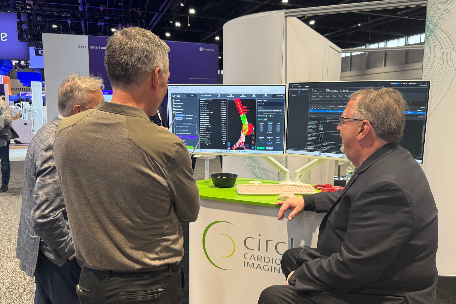 Three professionals discuss medical software on two large monitors at a Circle Cardiovascular Imaging trade show booth.