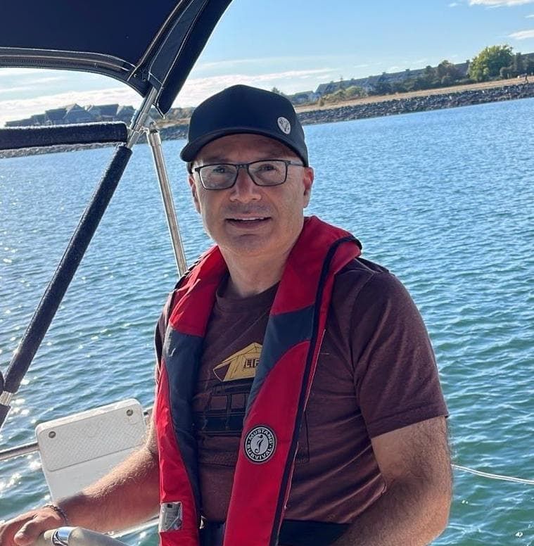 Man wearing a life vest and hat, steering a boat on a sunny day.