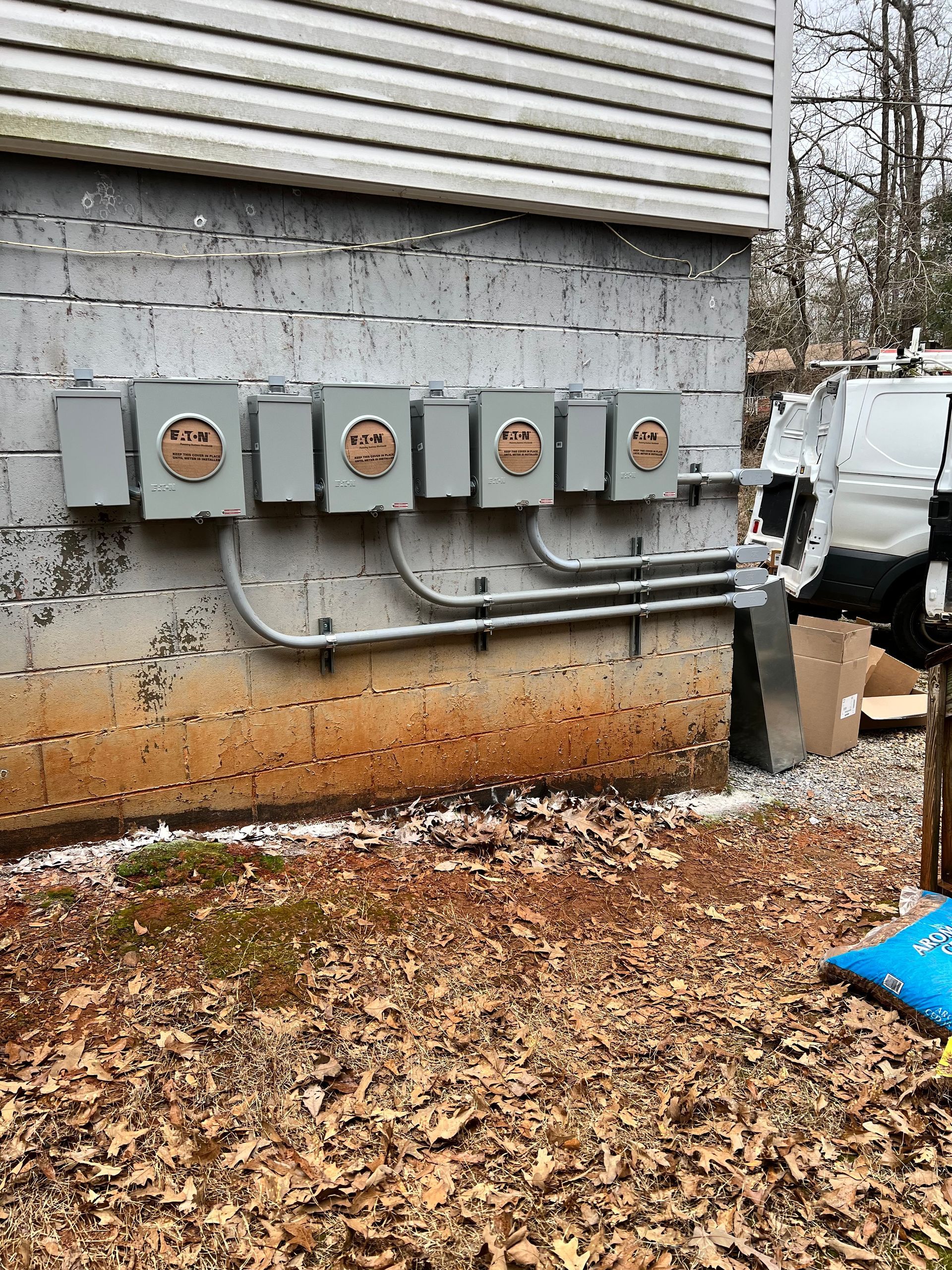 Gray electrical boxes on a cinder block building wall, with conduit running below.