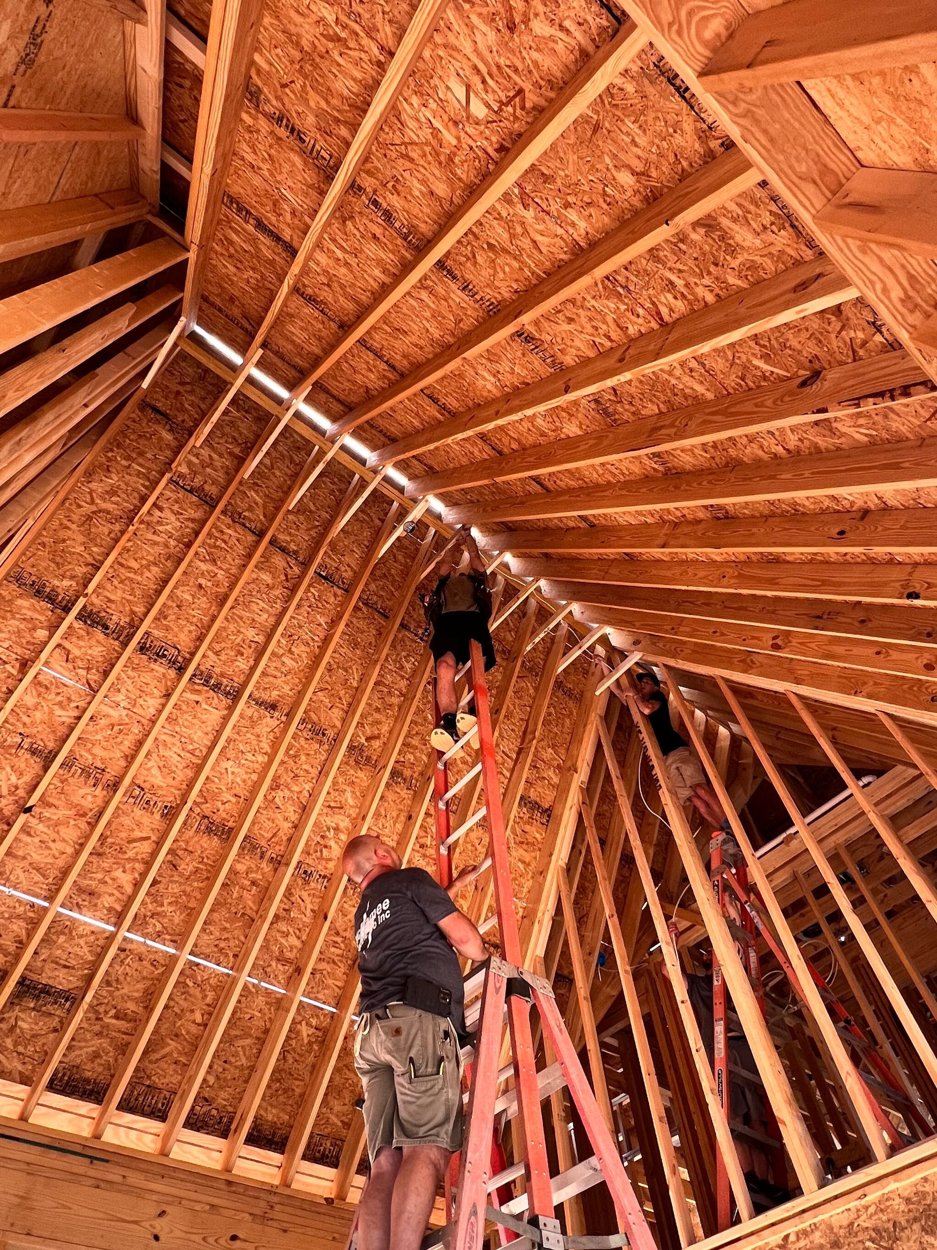 Construction workers on ladders inside a wood-framed roof structure, installing or repairing.