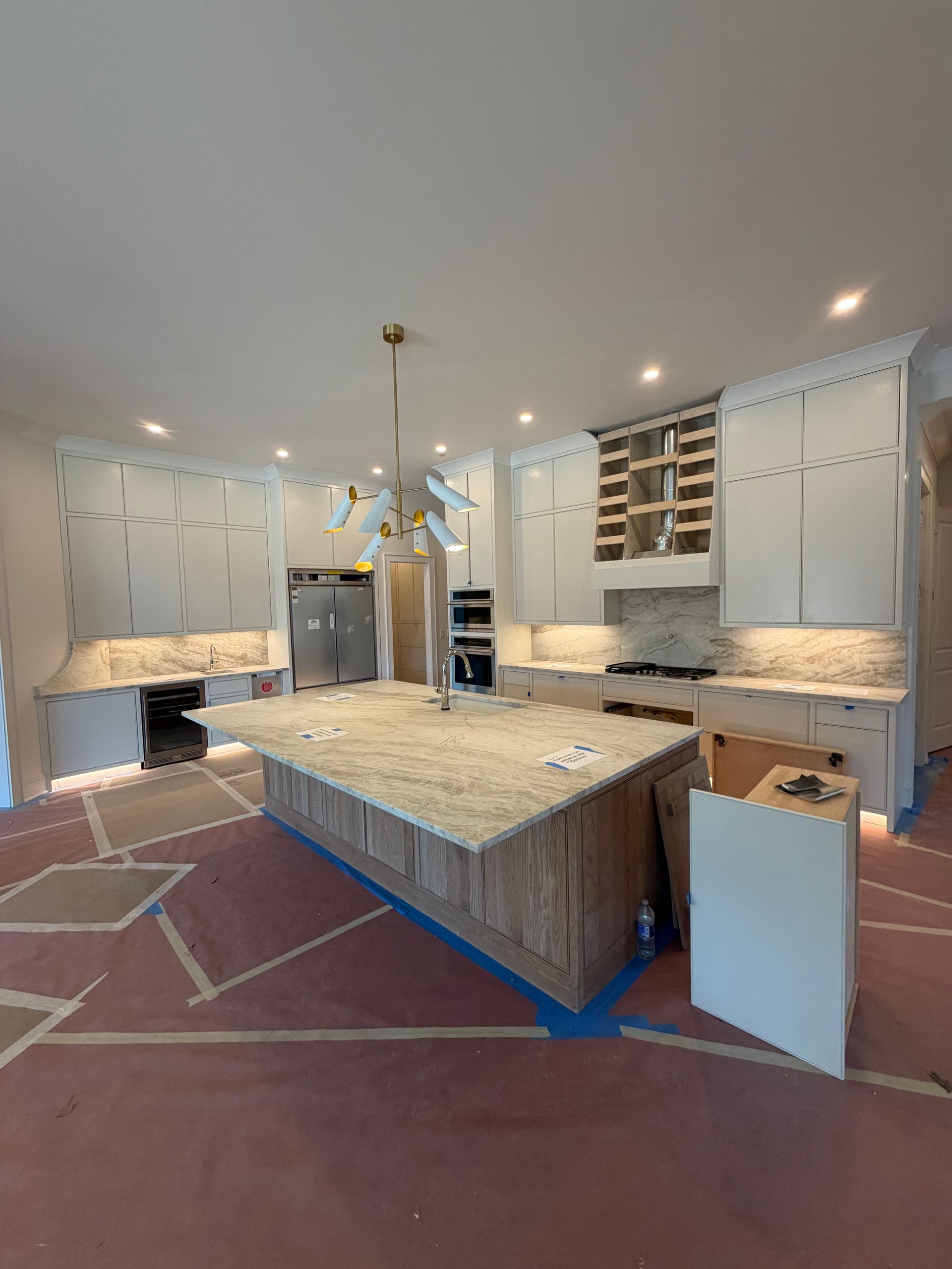 New kitchen with island, white cabinets, granite countertops, and flooring under construction.