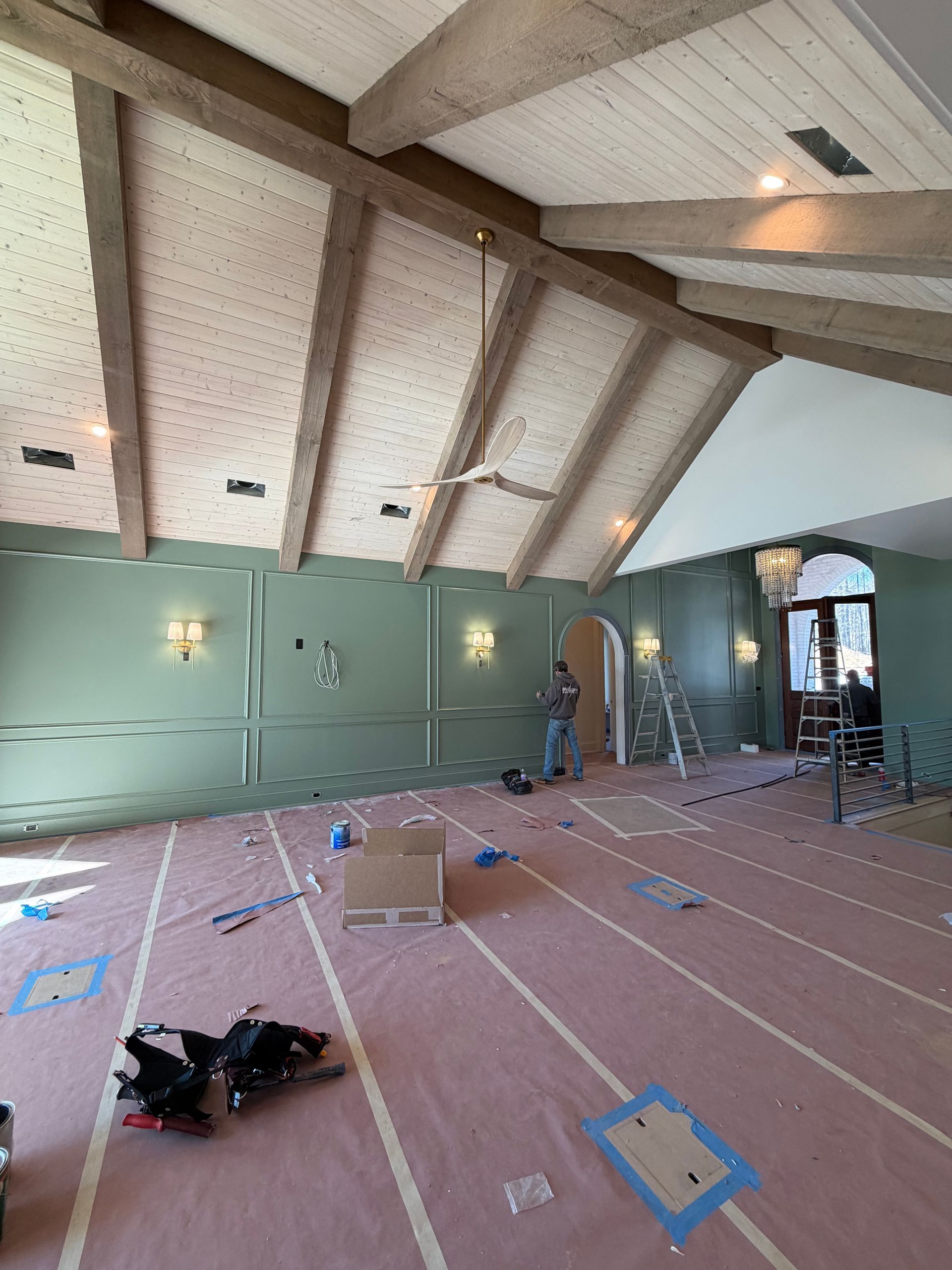 Room under construction, green walls, exposed beams, pink flooring, worker, ladders.