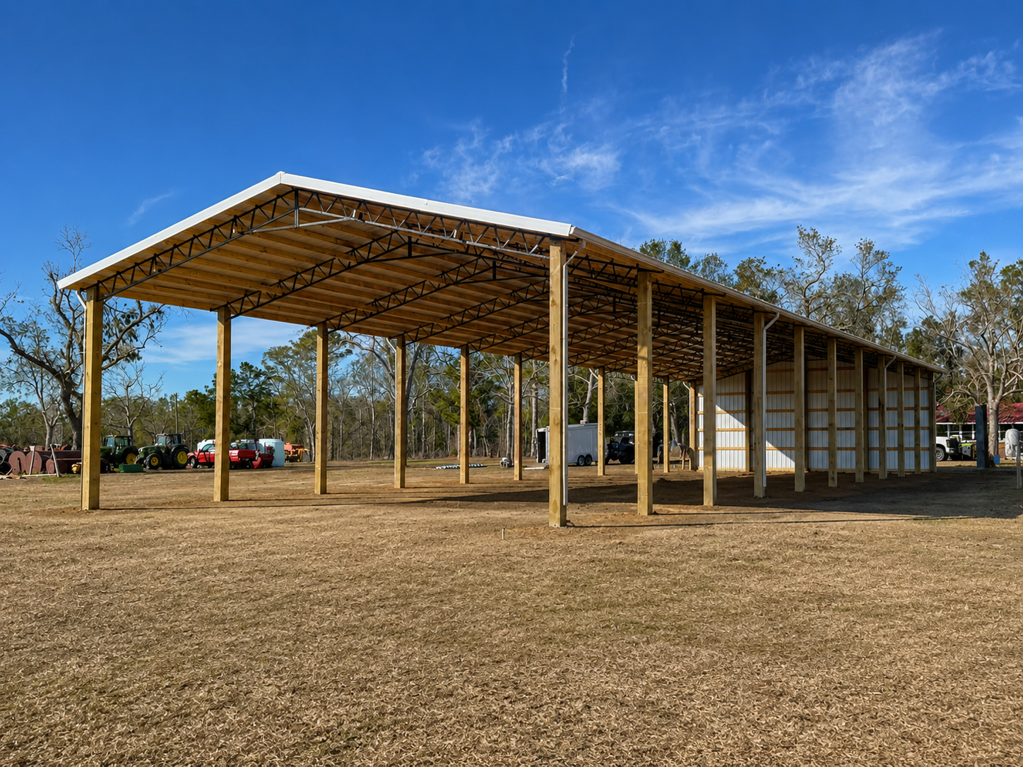 Carport with metal roof supported by wooden posts in a wooded area under a cloudy sky.