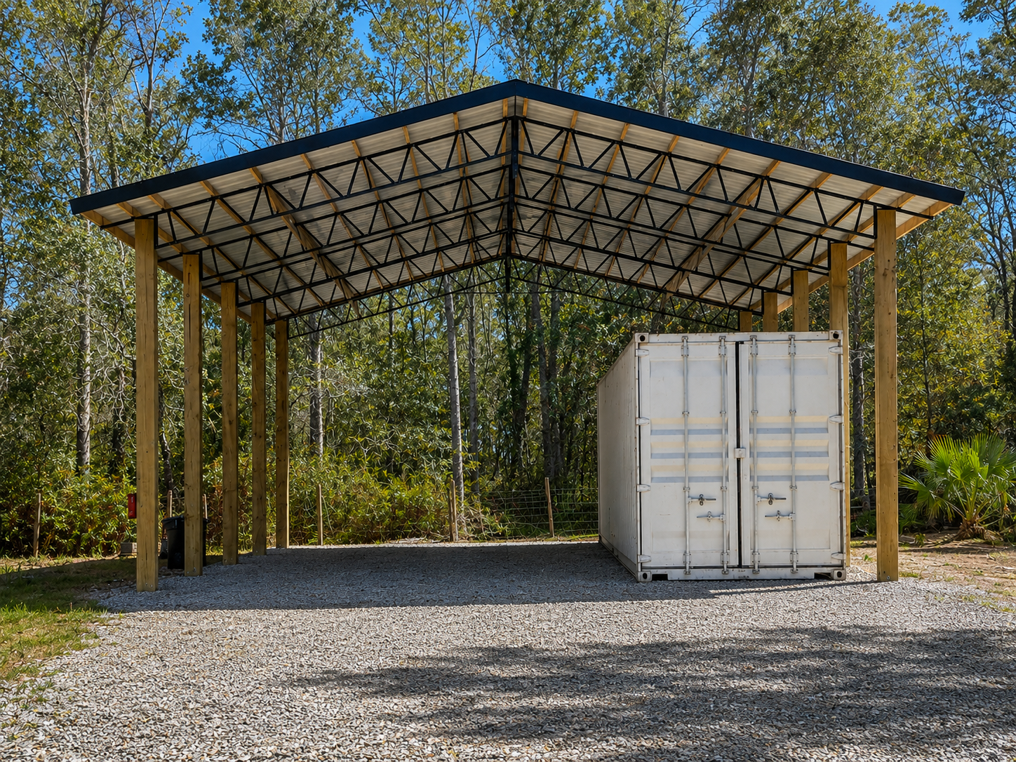 A large open-sided metal and wood pavilion on a grassy field under a cloudy sky.
