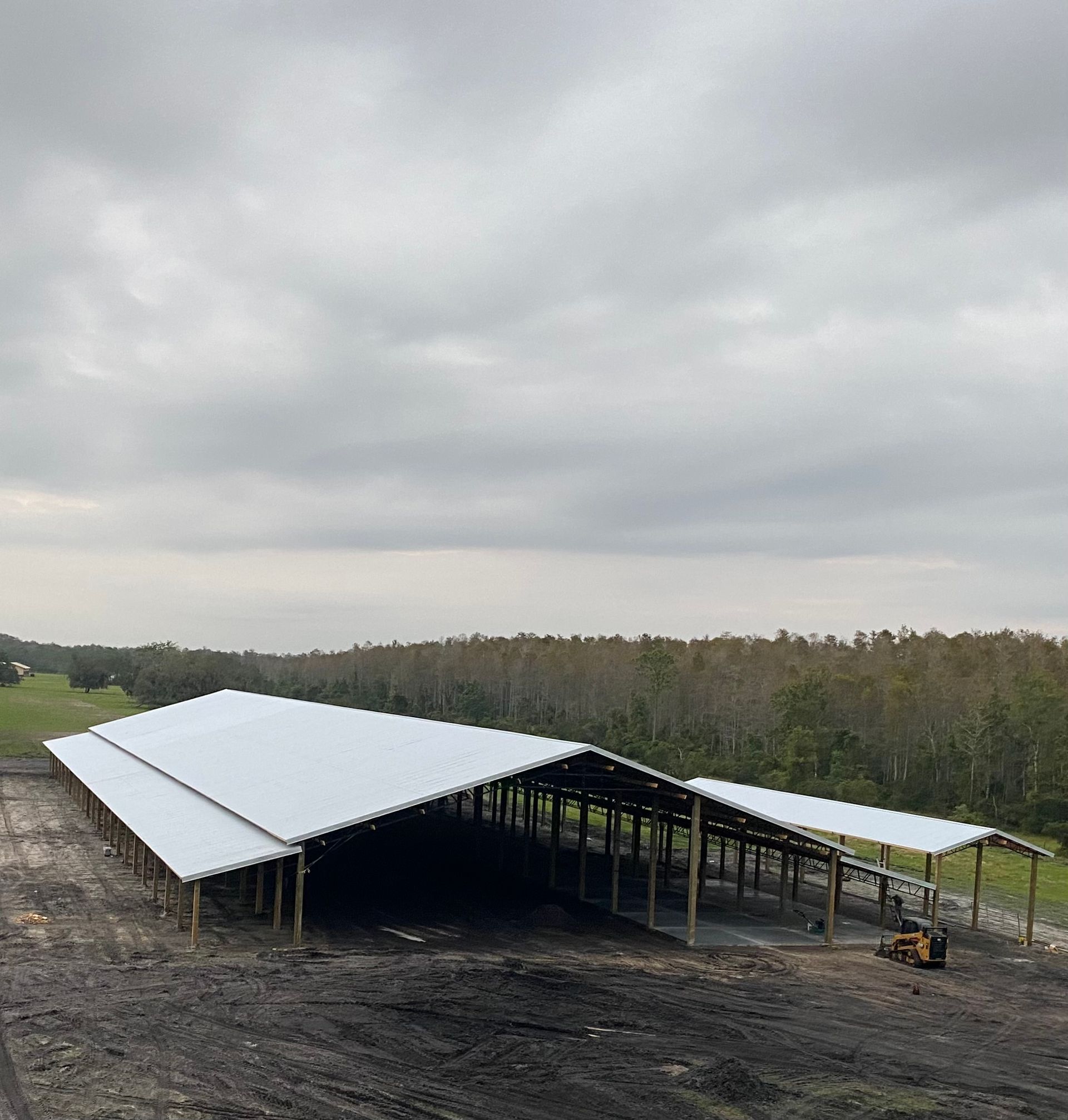 Wooden carport under construction in a wooded area with a small Bobcat on the left.