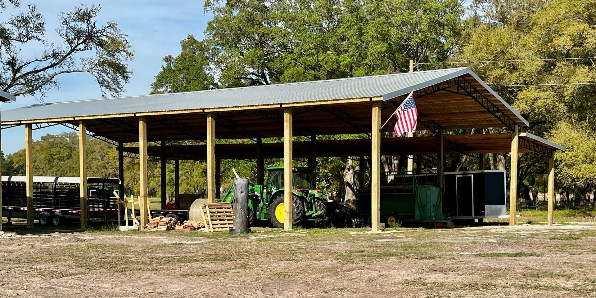A farm shed with a green tractor, trailer, and an American flag.