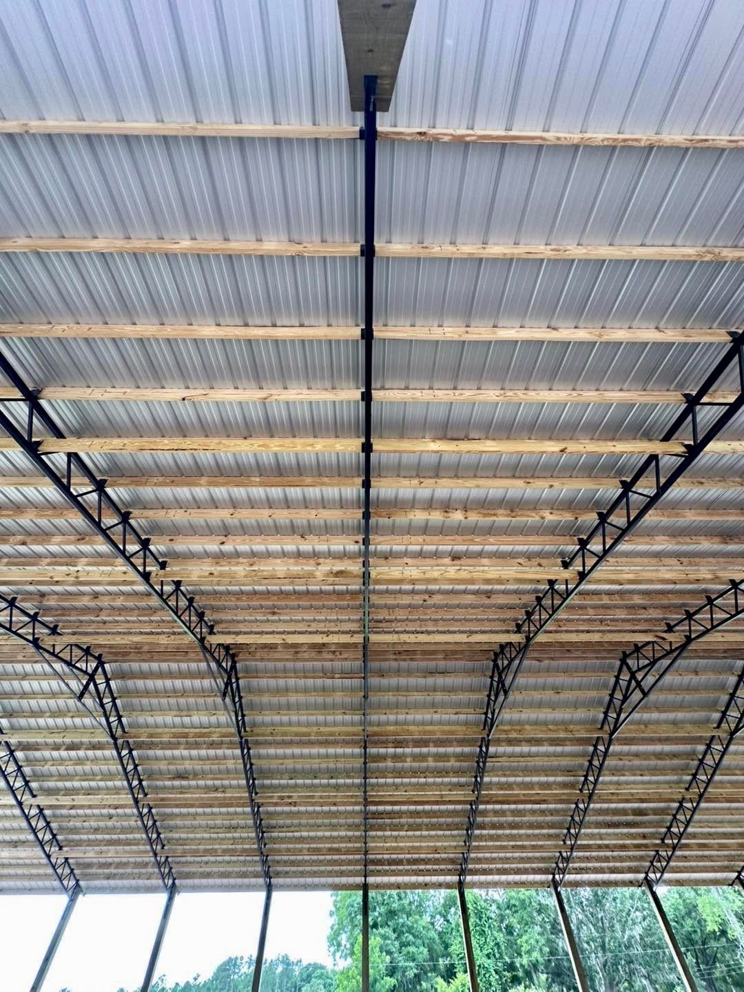 View from beneath a partially constructed roof structure with corrugated panels, wooden beams, and metal supports.
