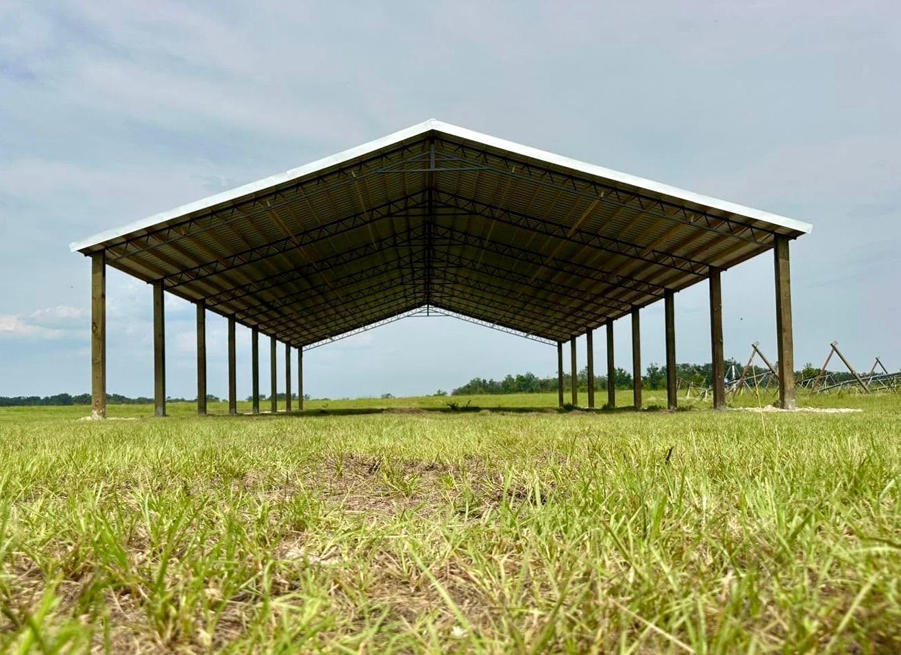 Large, open-sided barn with white roof and wooden supports in a grassy field under a cloudy sky.