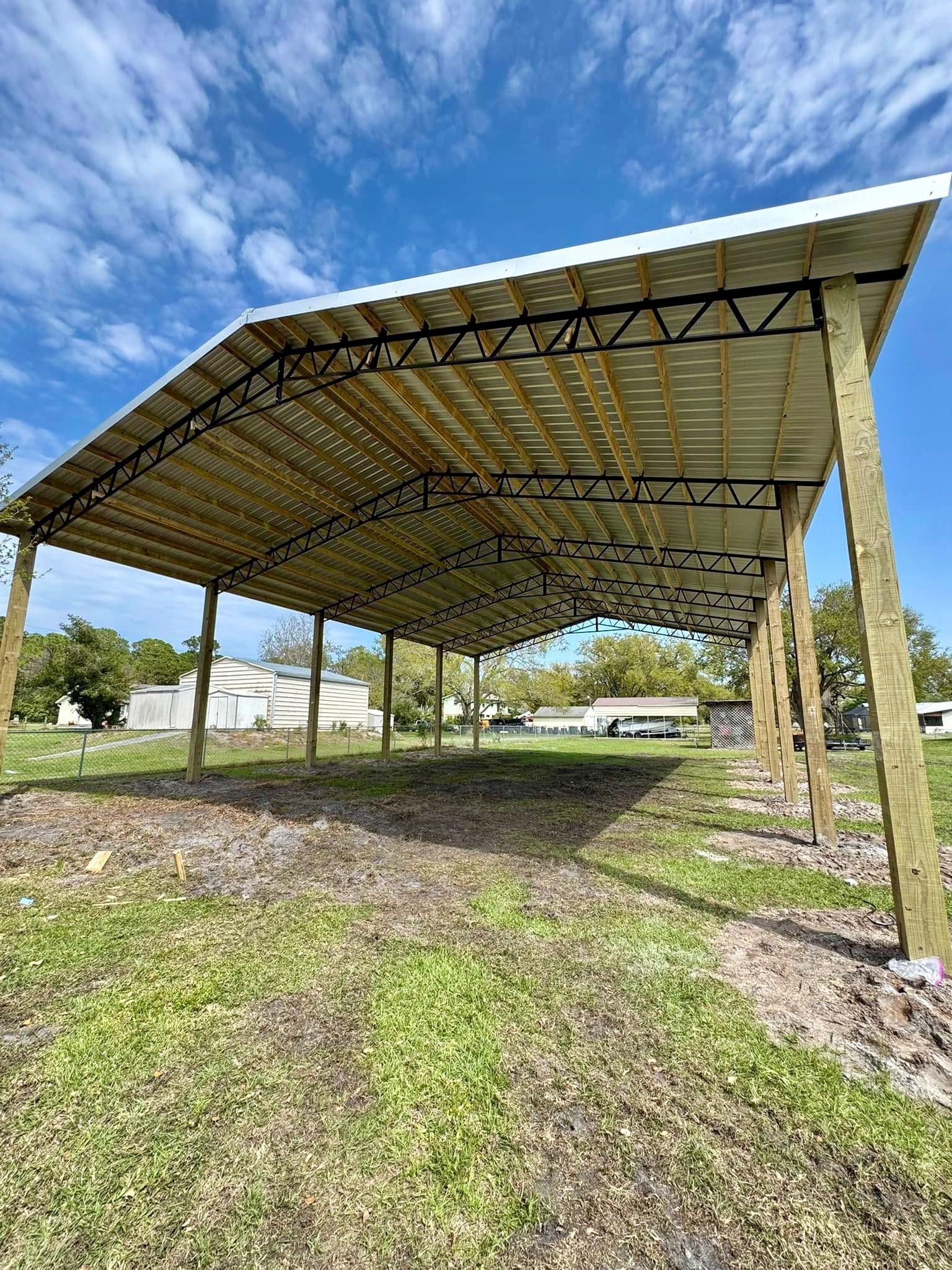 A metal and wood carport under a blue sky, on a grassy plot of land.