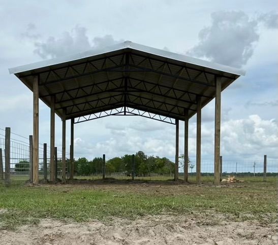 A large open-sided metal and wood pavilion on a grassy field under a cloudy sky.