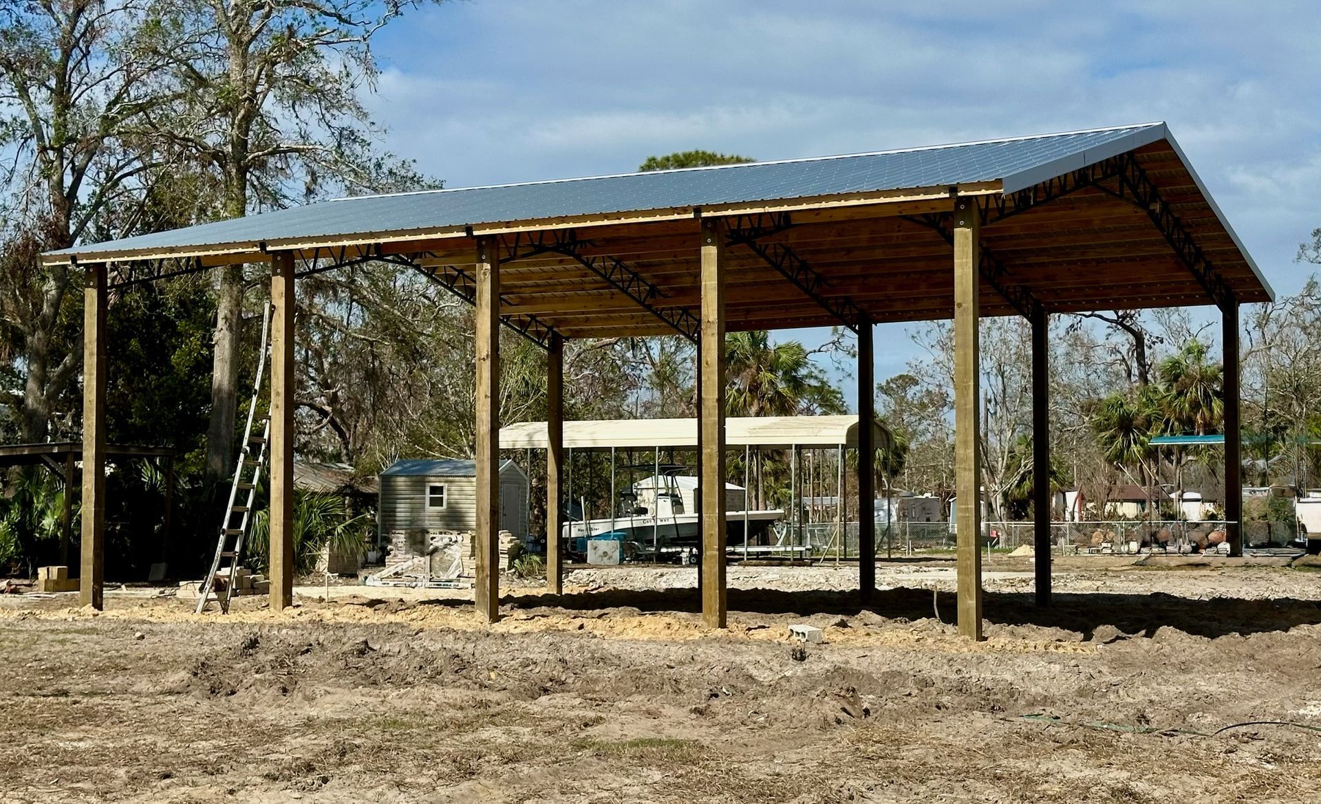 Wooden carport with corrugated metal roof under construction in a dirt lot.