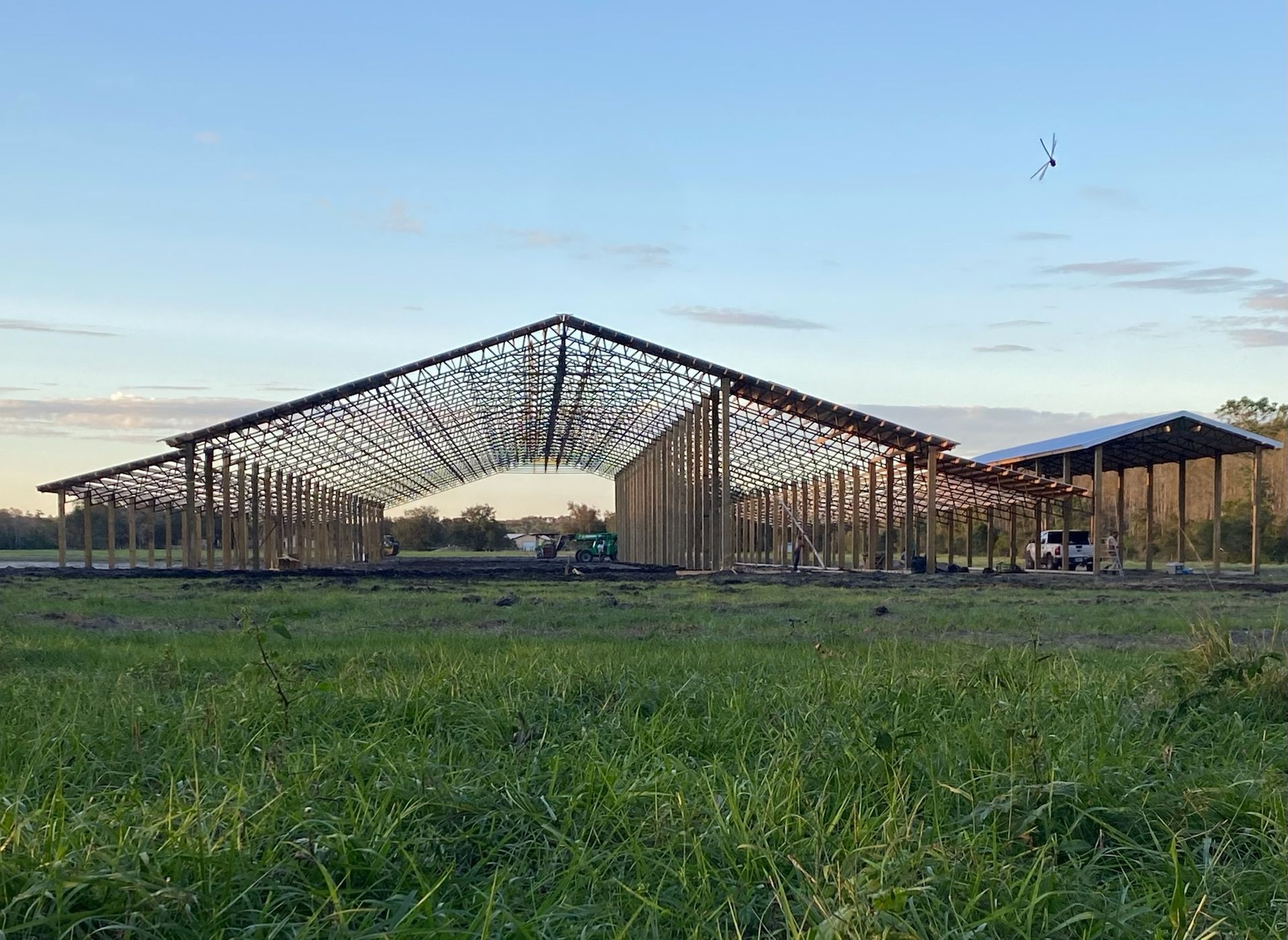Steel frame of a large building under construction in a grassy field.