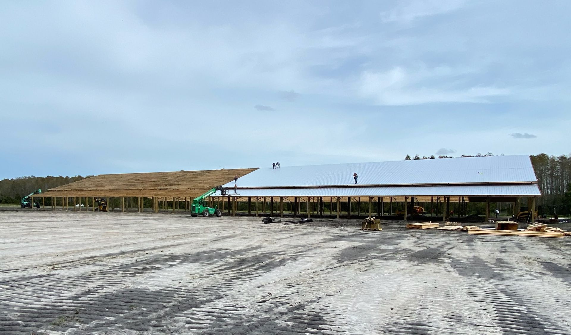 Construction site with a long, partially built wooden structure under a cloudy sky.