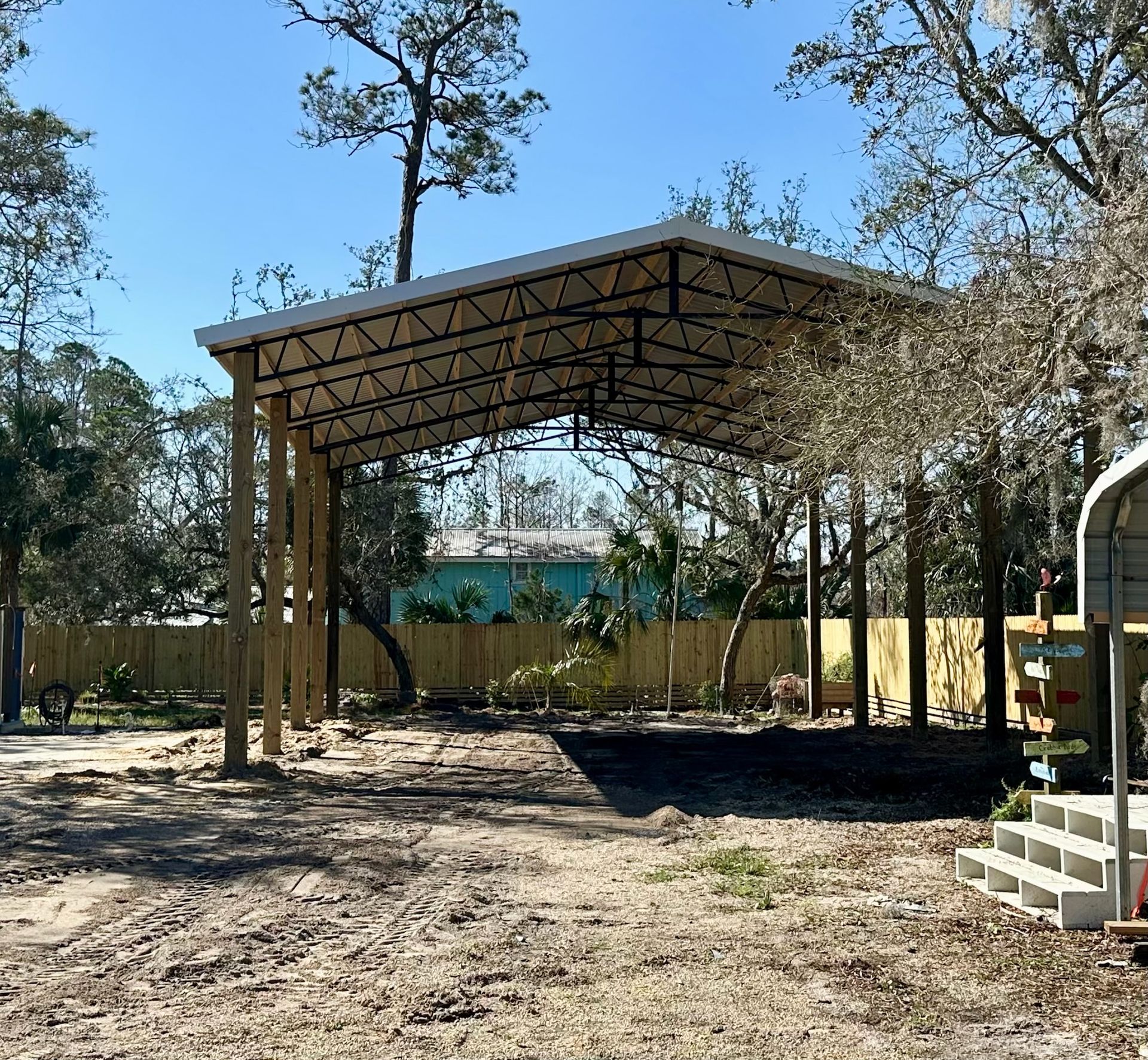 Carport with metal roof and wooden supports in a yard with trees.