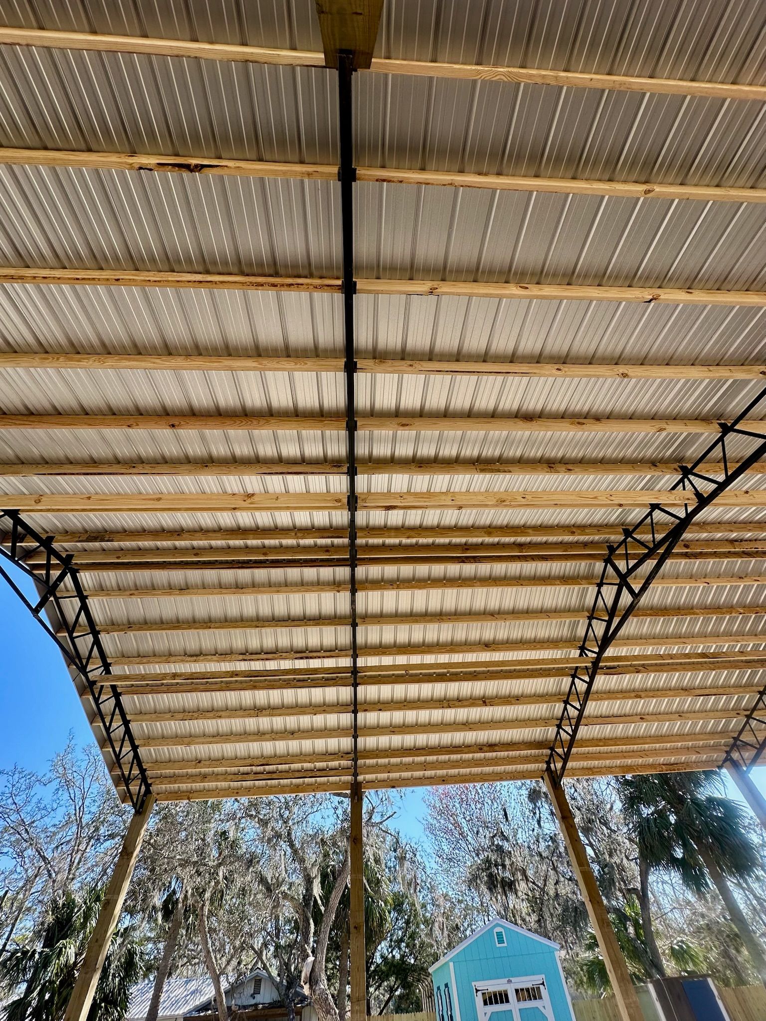 View from below of a wood-framed metal roof with a black pipe running down the center.