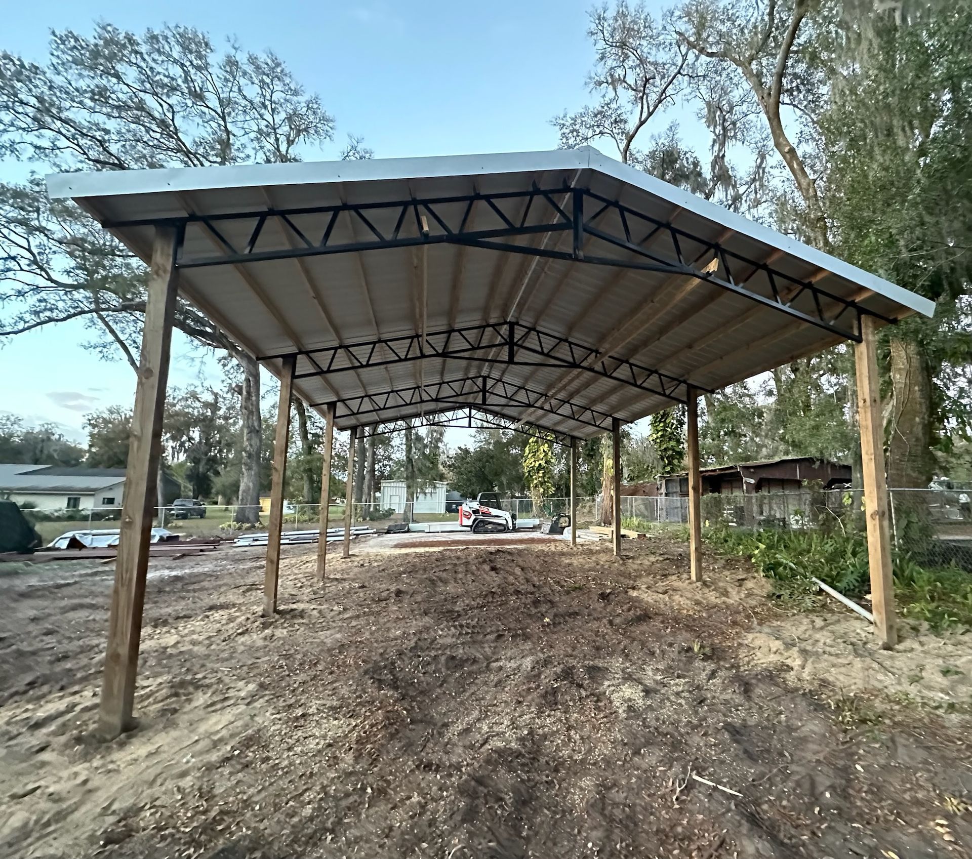 Metal carport with wooden posts, in a dirt yard.