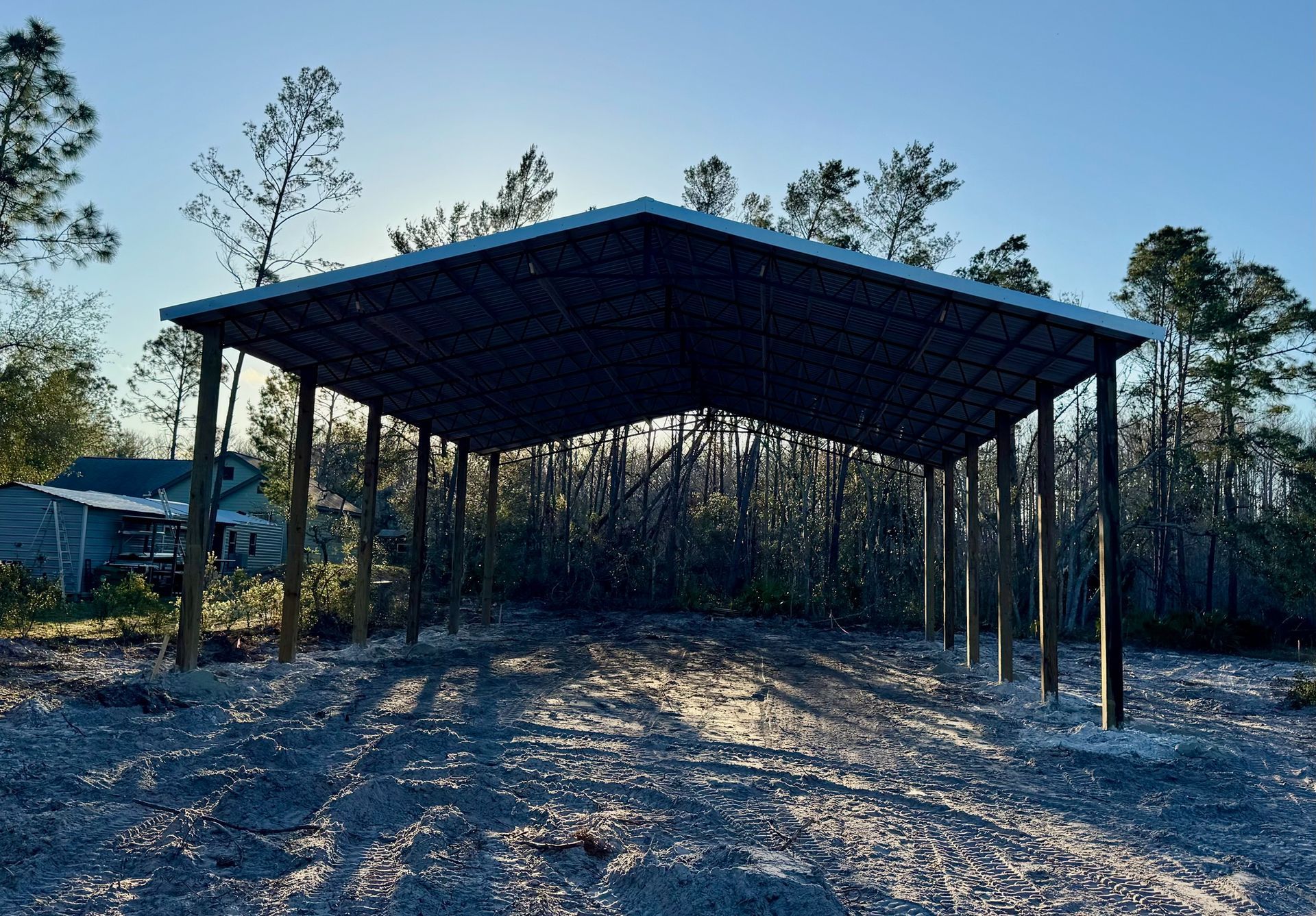 Carport with metal roof in a clearing, sunlight shining through trees in the background.