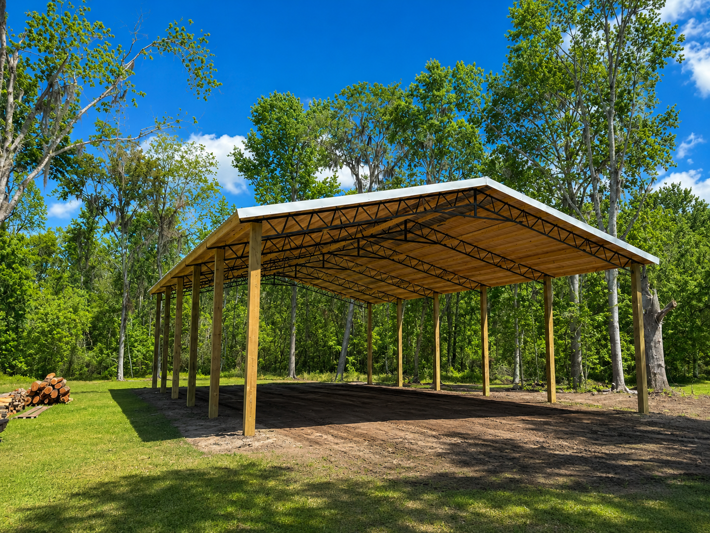 Open-air metal building with a concrete floor, supported by wooden posts, under a blue sky.