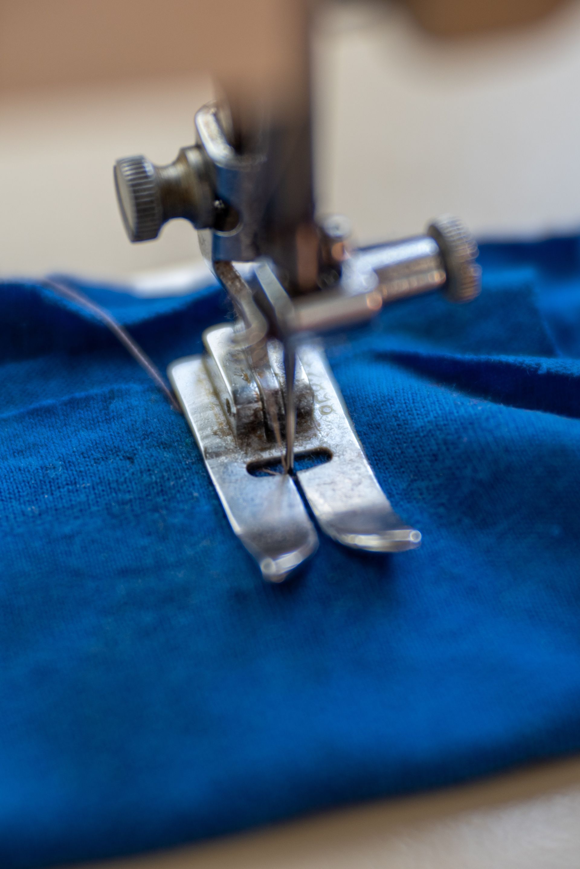 A close up of a sewing machine stitching a piece of blue fabric.