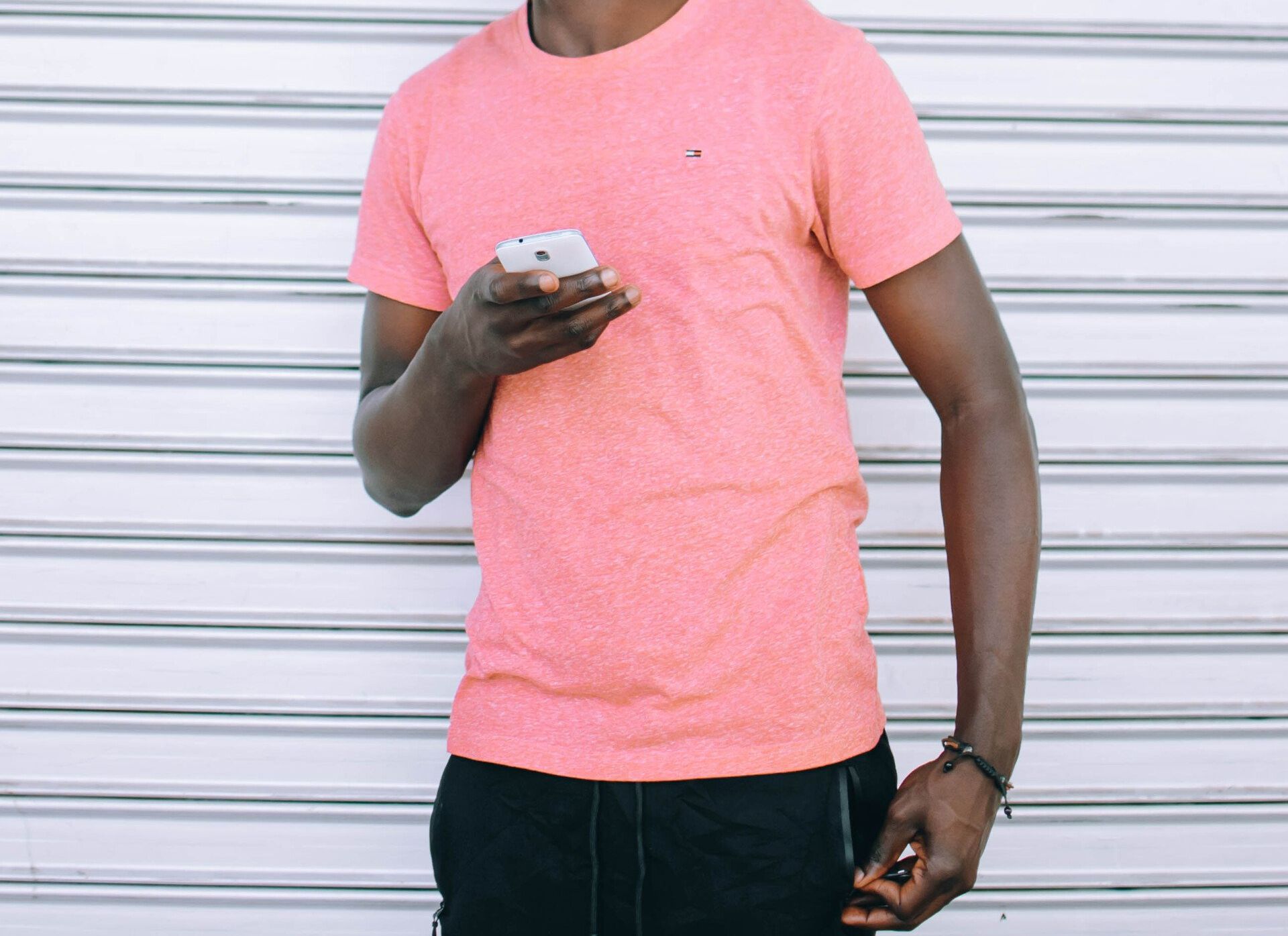 A man in a pink t-shirt is holding a cell phone.
