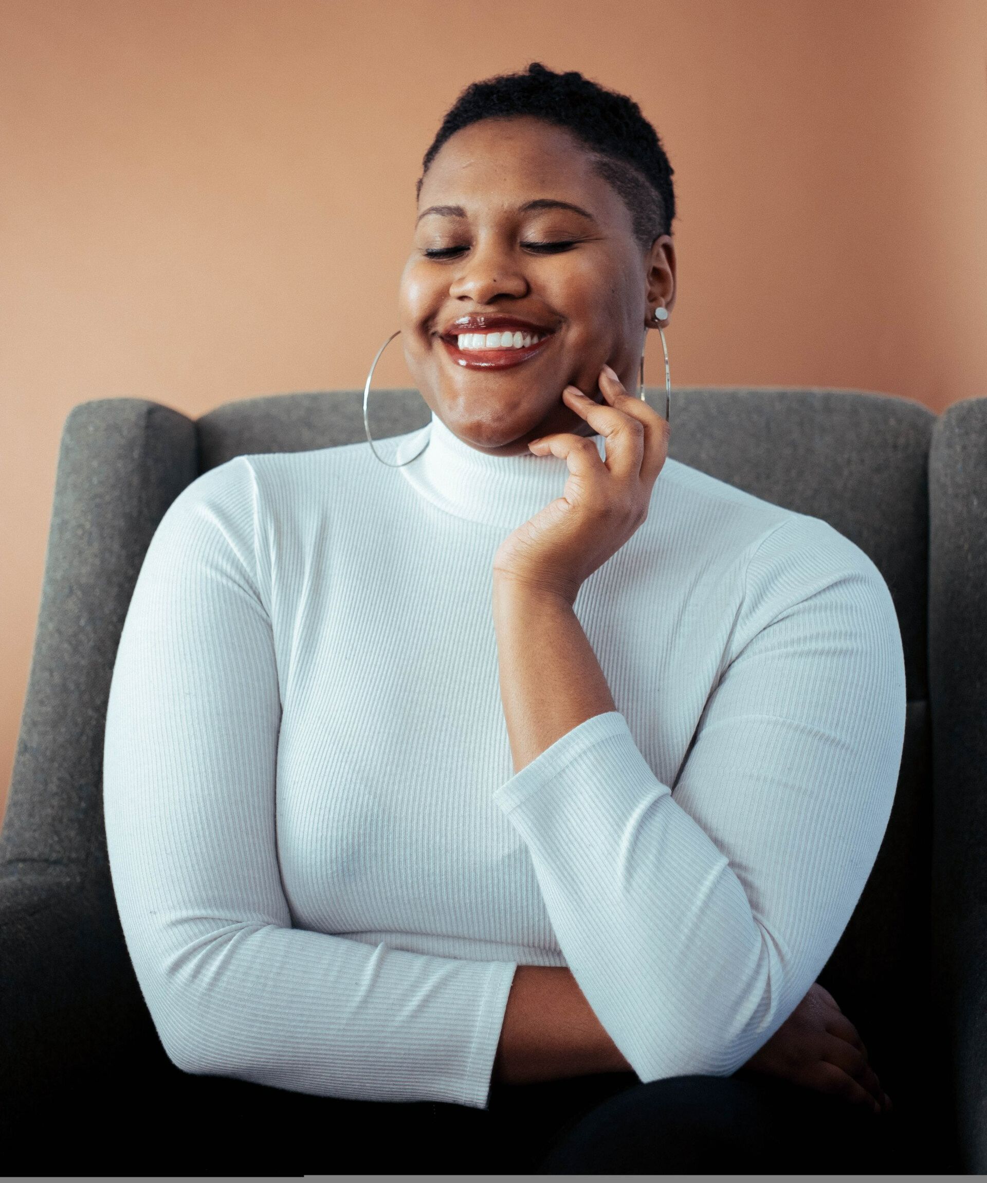 A woman in a white turtleneck is smiling while sitting in a chair