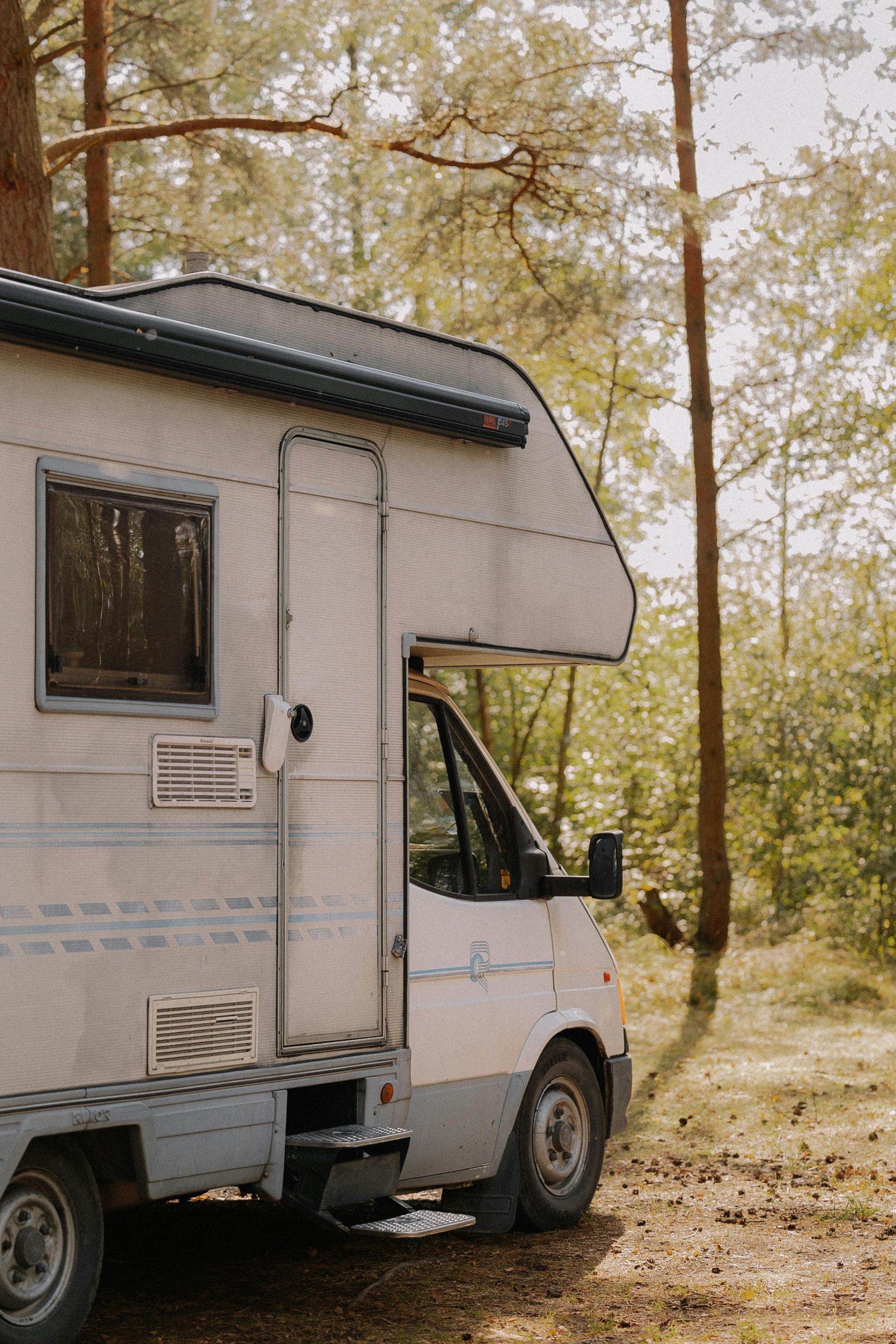 A white rv is parked in the middle of a forest.