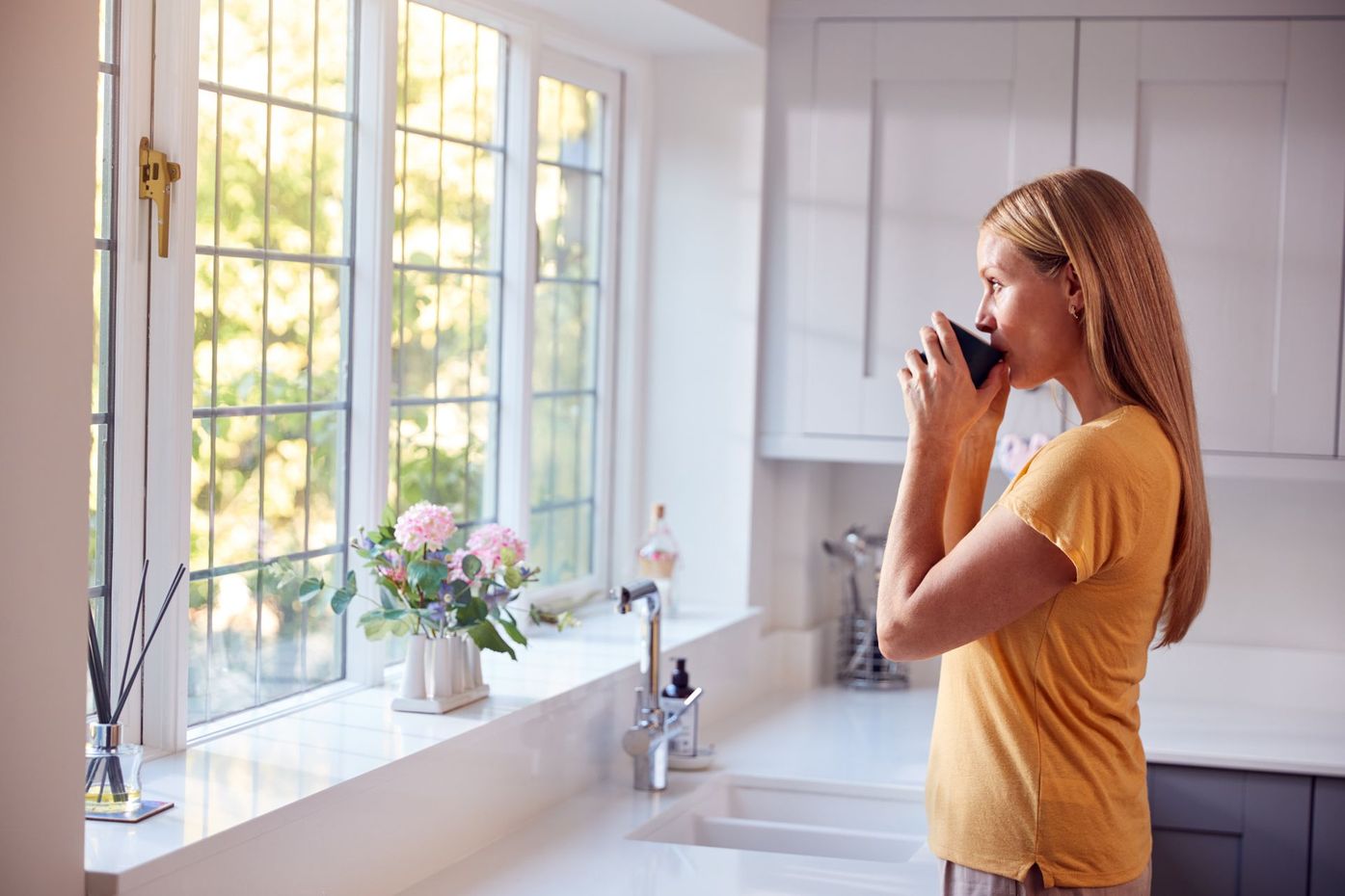 A woman is drinking a cup of coffee in a kitchen.