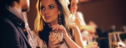 Woman holding a drink and talking to someone at a bar.