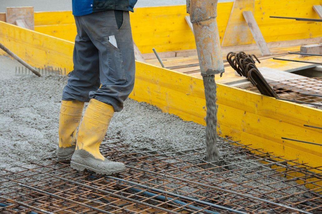 Worker pouring concrete into a bright yellow wall form.