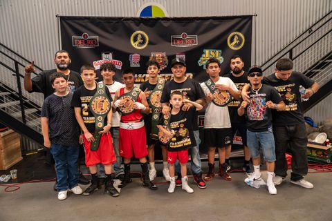 Group of young boxers with championship belts pose in front of a banner.