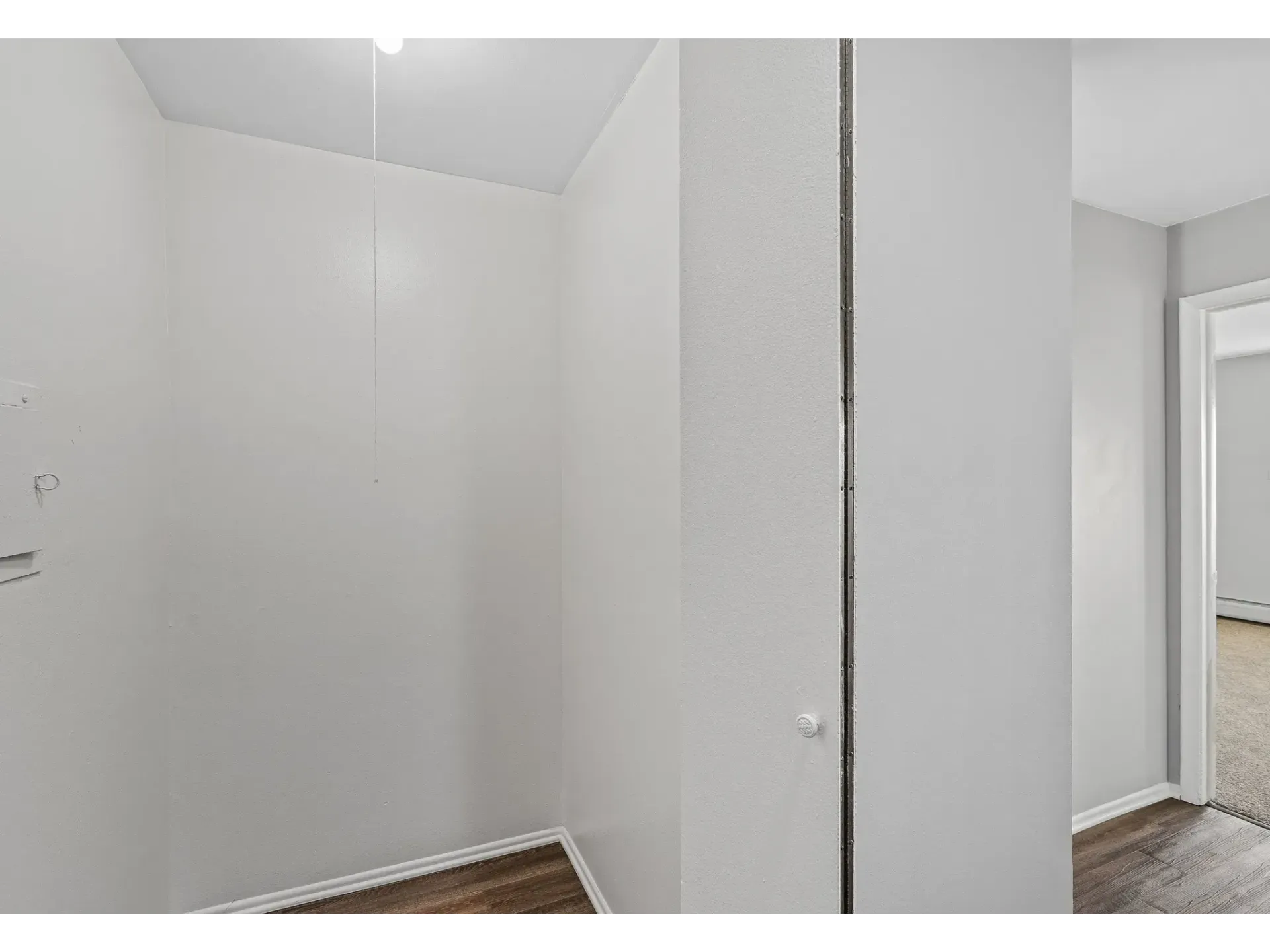 Interior view of an apartment hallway with white walls and wooden flooring