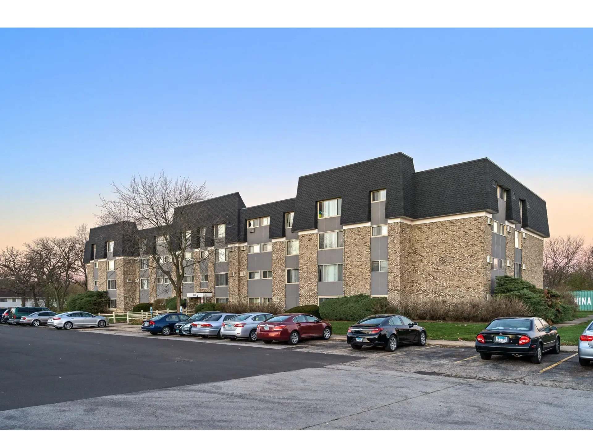 Exterior view of a residential apartment building with parking lot and trees