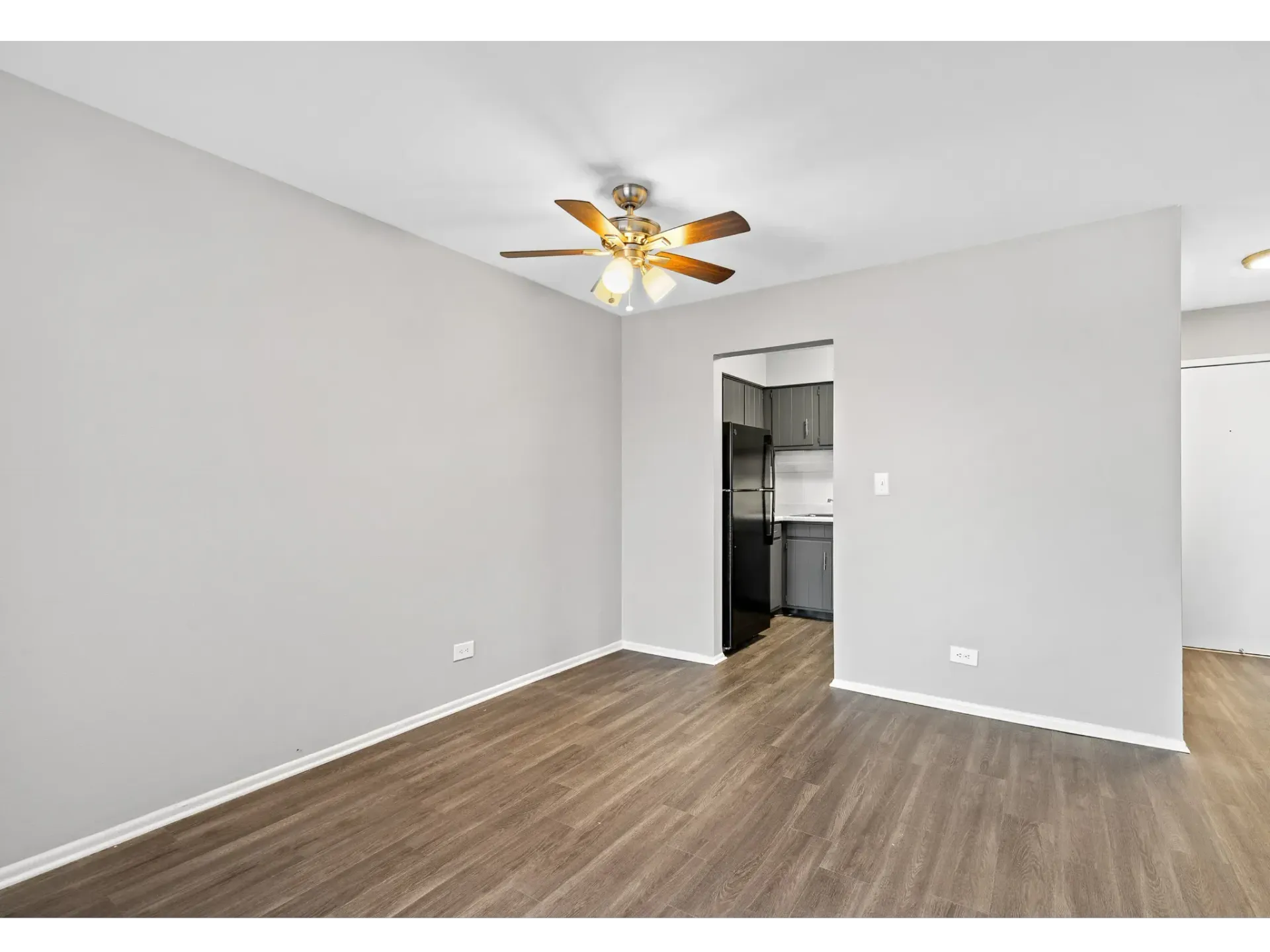 Interior view of an apartment living space with a ceiling fan and kitchen access.