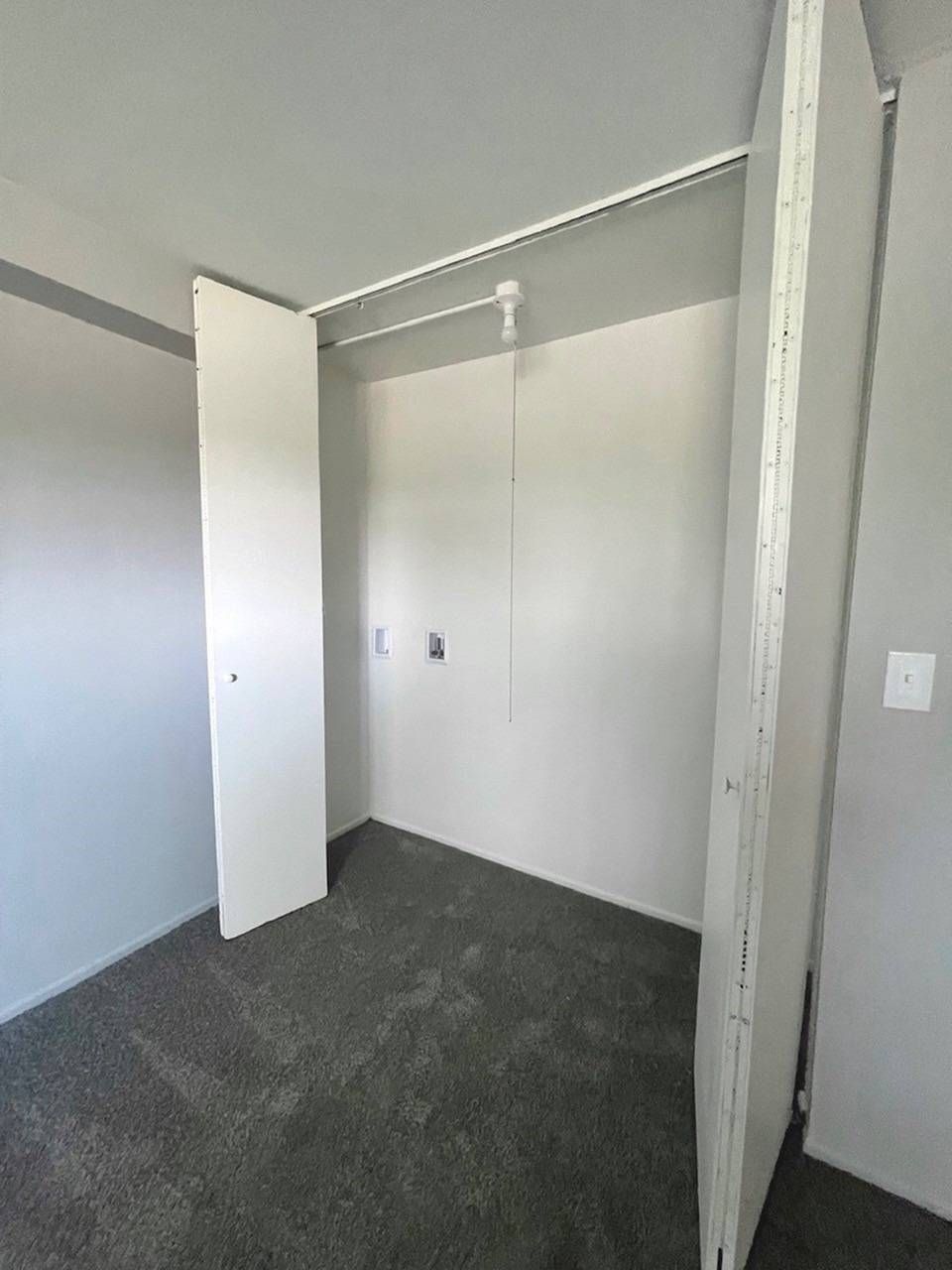 Empty closet with white walls, open door, and dark carpet in a small room