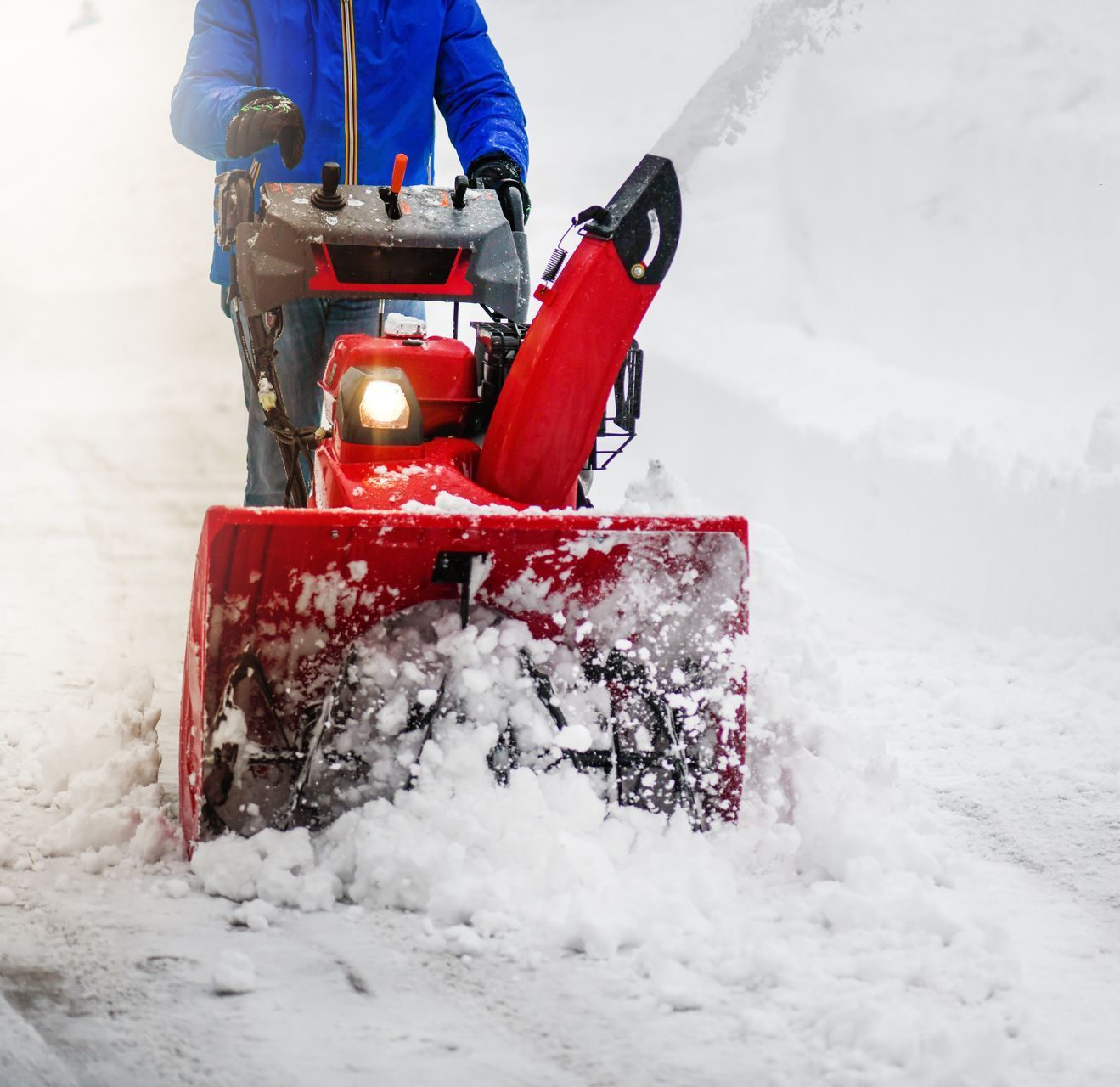 A man is using a red snow blower to clear snow from a sidewalk.