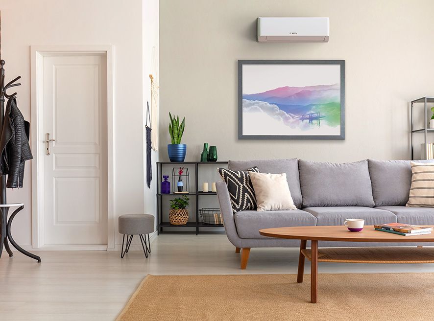 A modern living room with a grey sofa, wooden coffee table, framed abstract wall art, and a wall-mounted air conditioner.