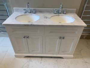 A white double-sink bathroom vanity with a marble countertop, set against a wall with silver heated towel racks.