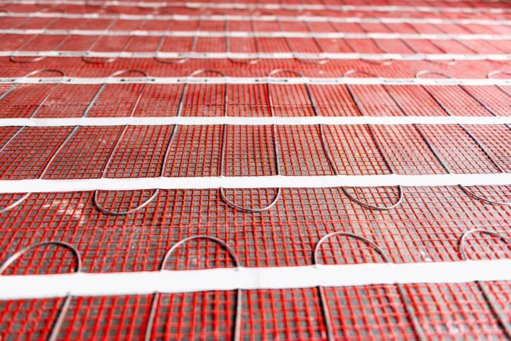 Radiant floor heating cables installed on a red mesh backing before being covered by flooring materials.