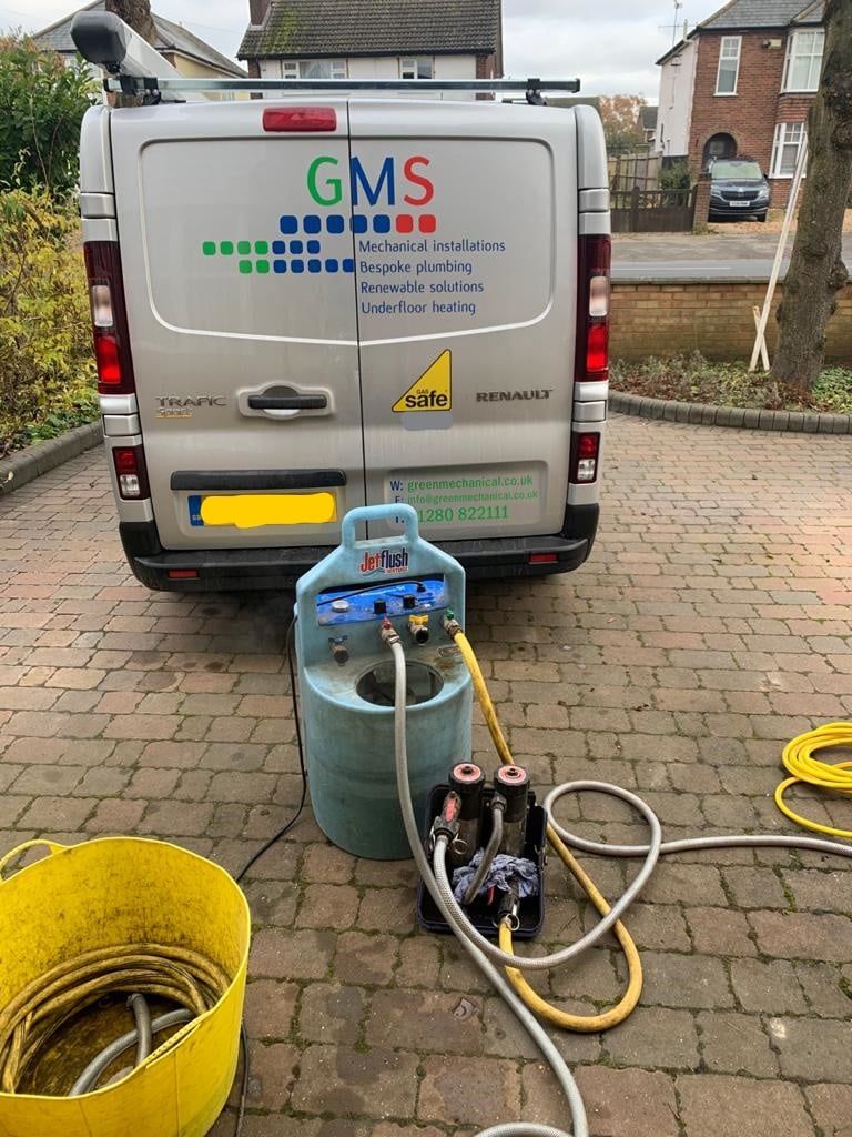 A silver utility van parked in a driveway, connected to a mobile pressure washing or cleaning system on the ground.