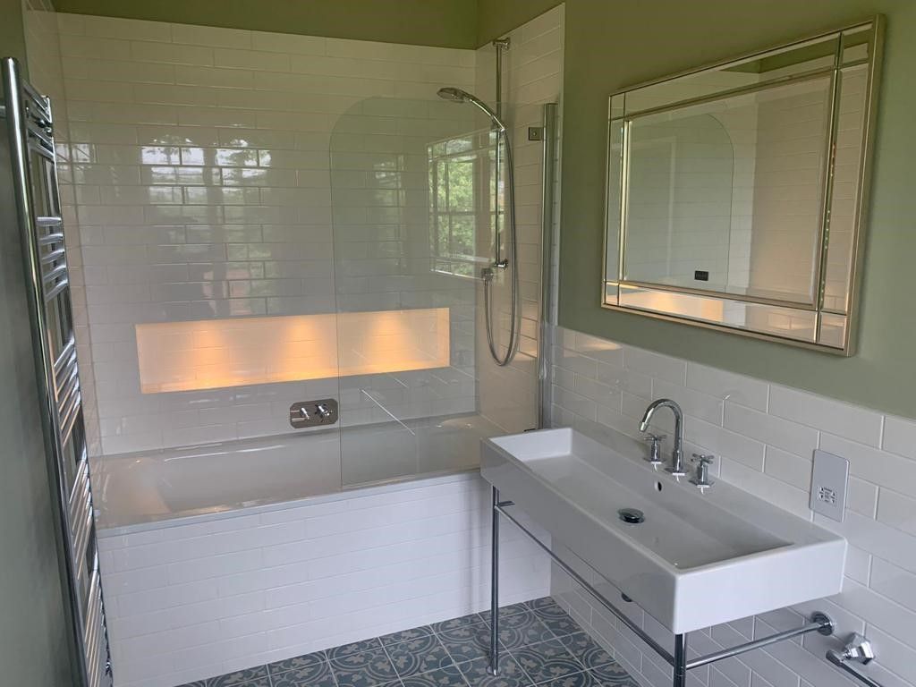 A modern bathroom featuring a white porcelain tub with a glass screen, a pedestal sink, and a decorative mirror.