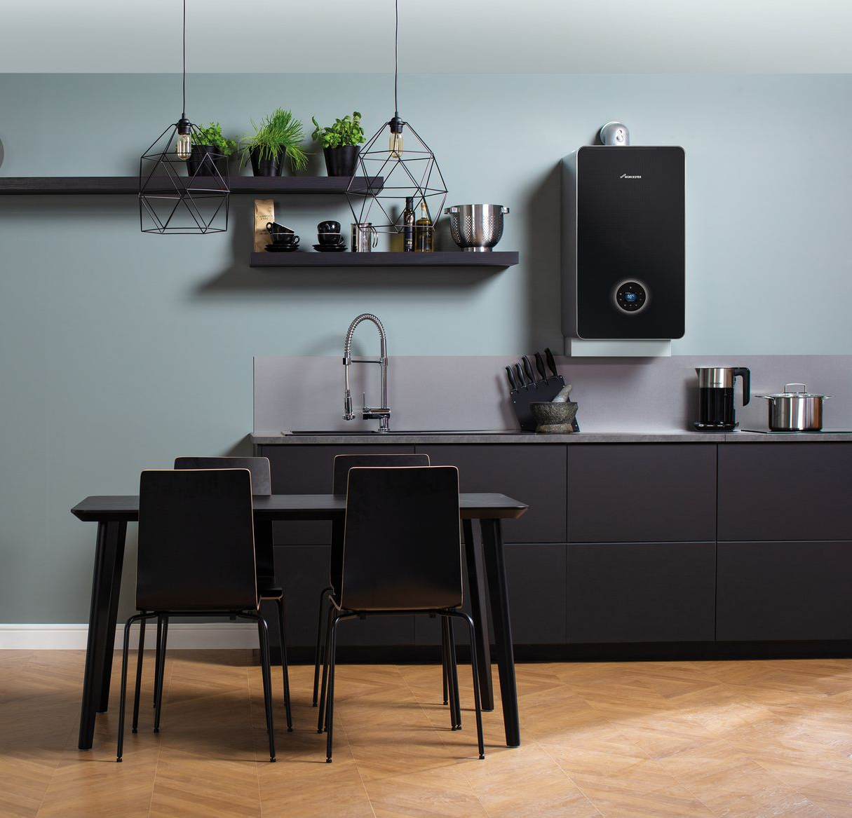 Modern kitchen with matte black cabinetry, a sleek wall-mounted boiler, two black chairs, and floating shelves with plants.