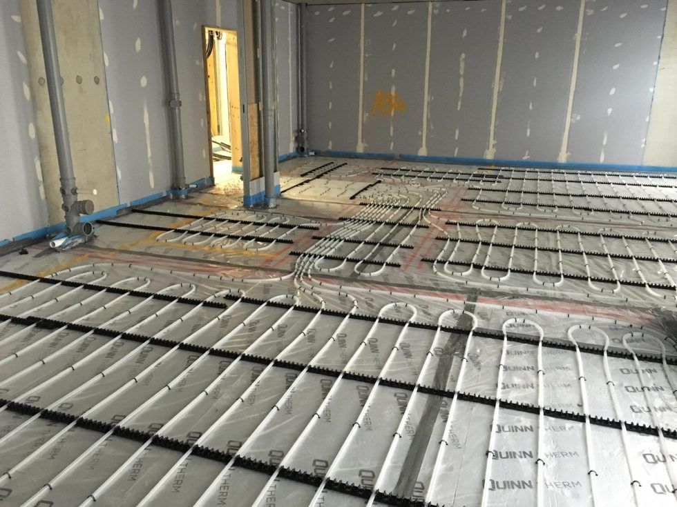 Radiant floor heating pipes installed on a concrete subfloor in a room under construction with unfinished drywall walls.
