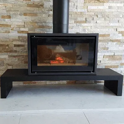 A modern black wood-burning fireplace insert sits on a black bench against a beige, textured stone accent wall.