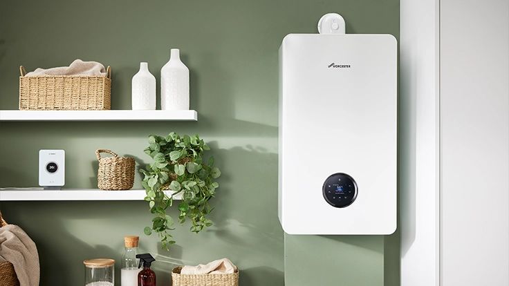 A modern white wall-mounted boiler in a room with sage green walls, wooden shelves, a plant, and home decor items.